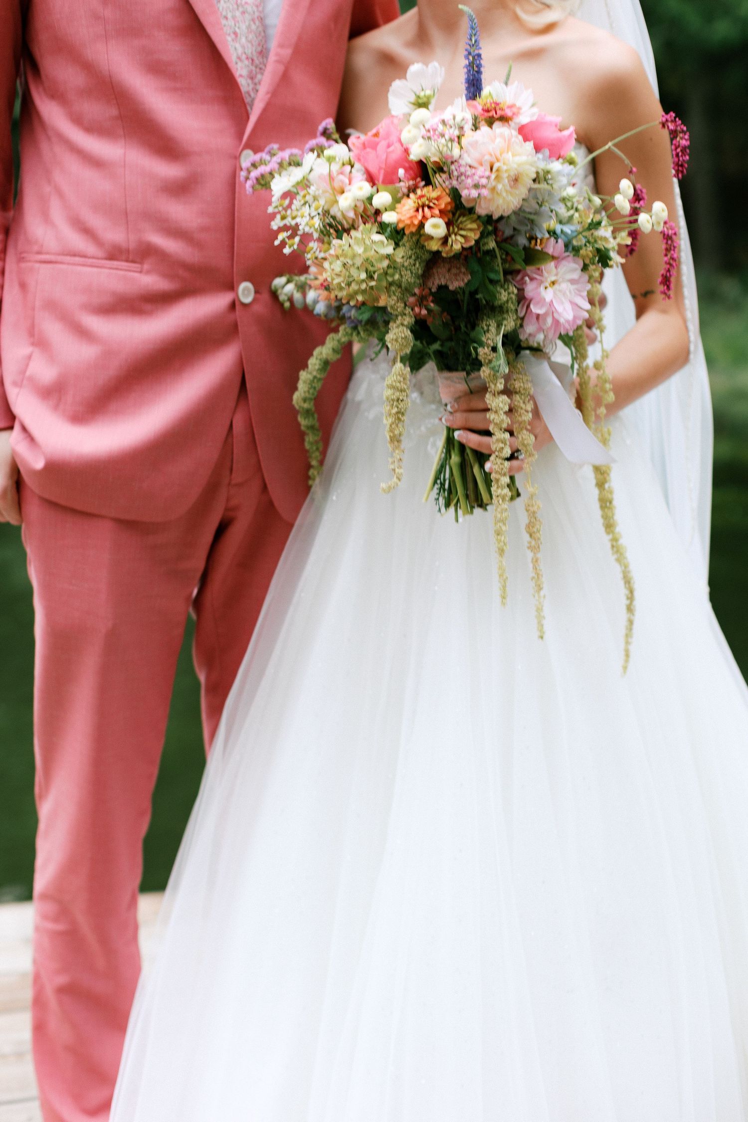 Bride and groom detail shot showing coral suit, white dress and pastel floral bouquet-Adrianna Elizabeth Photography.