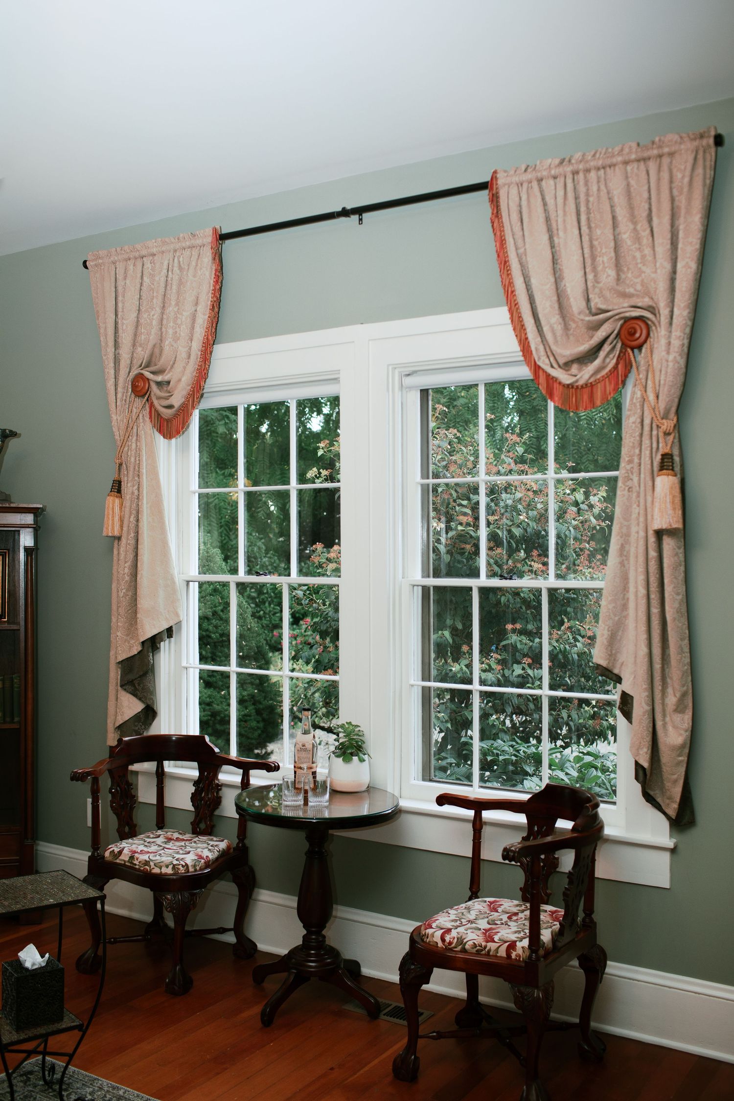 A series of windows in a room with mint green walls, hardwood floors, and peach-colored curtains.