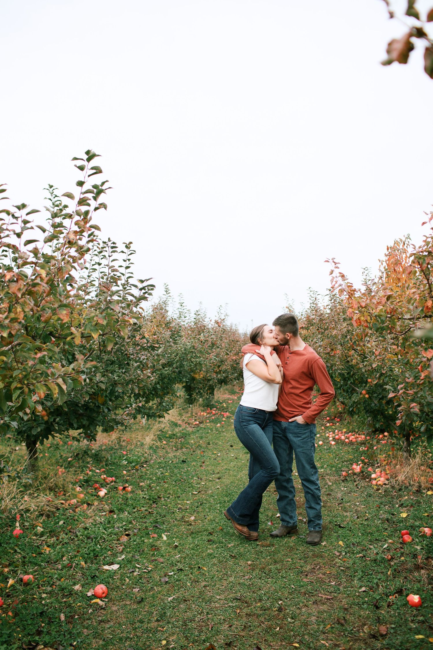 A couple embraces and dances playfully in an autumn apple orchard with red fruit on the trees.