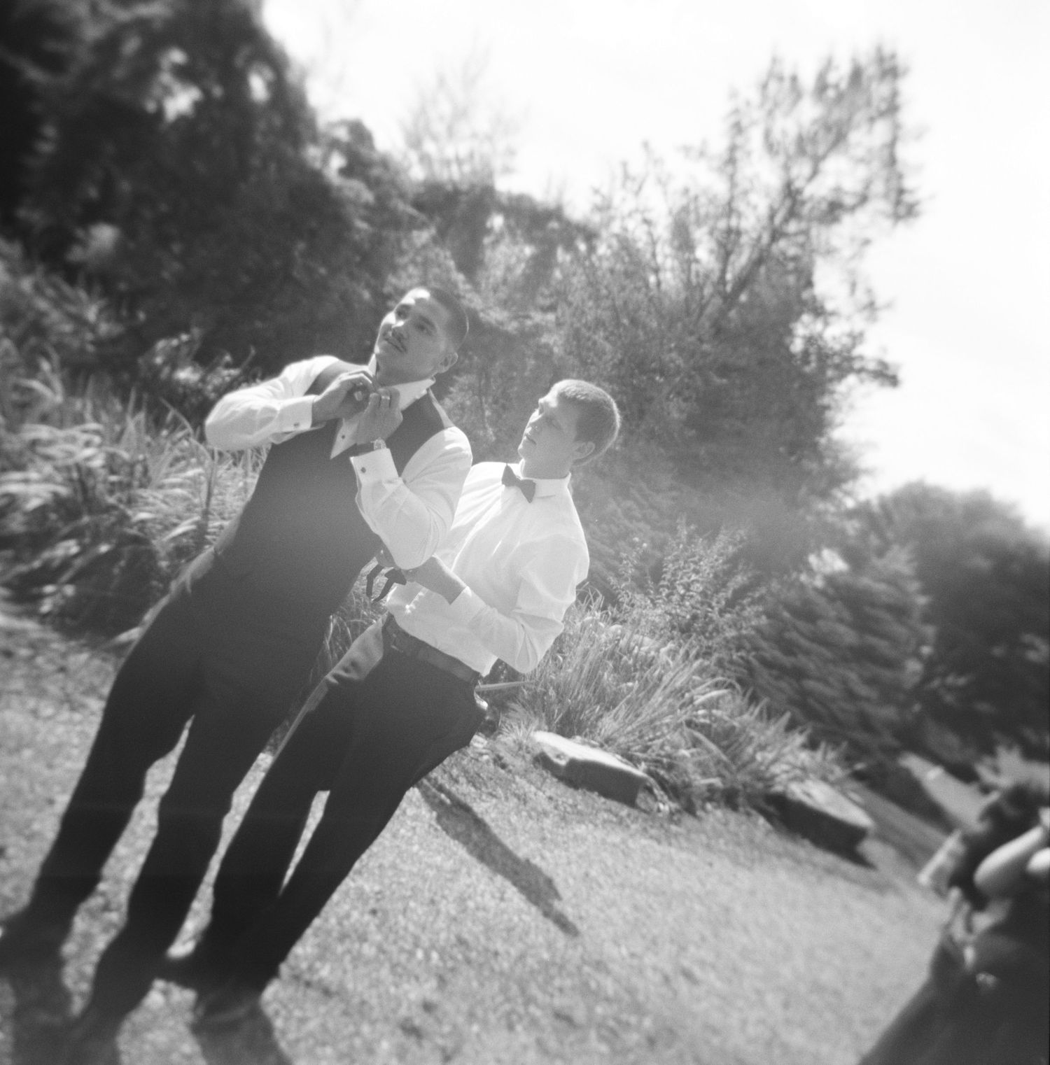 Groom posing outdoors in a black and white photo series with sunlight filtering through trees on 120 medium format film.