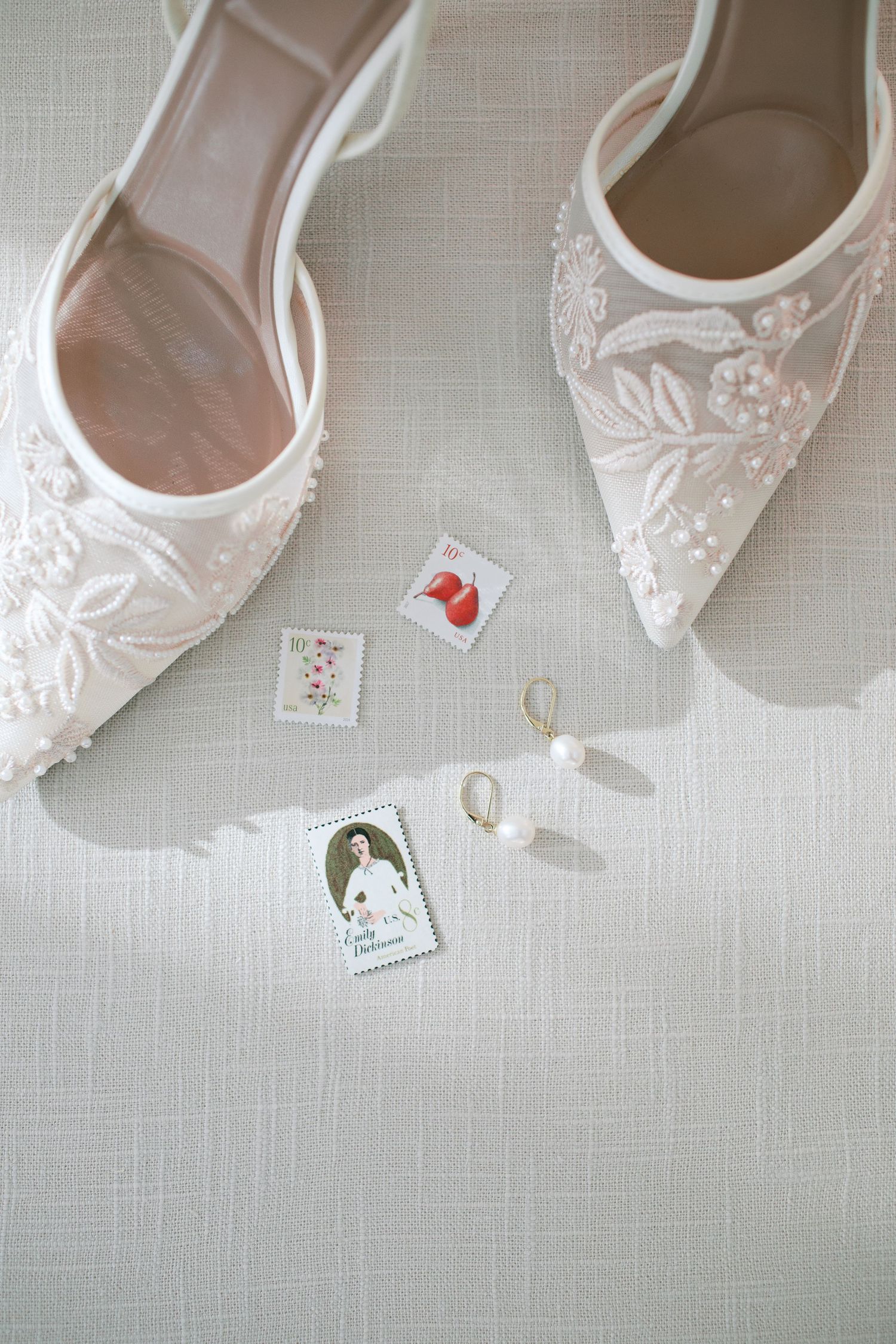 Elegant white lace bridal shoes with delicate embroidery displayed alongside small decorative cards and earrings.