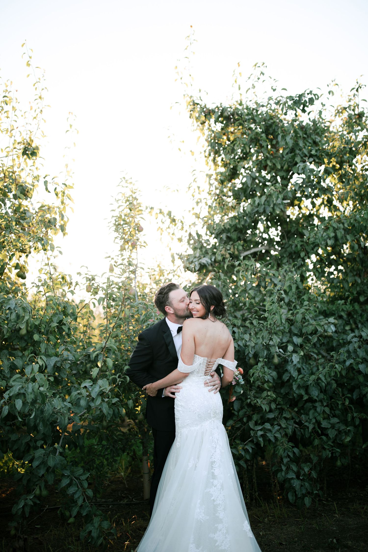 Romantic wedding couple shares a tender kiss in a lush garden setting during golden hour.