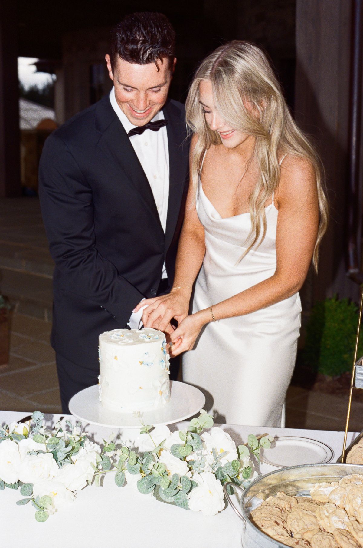 A couple in formal wedding attire cuts their wedding cake together in a series of candid reception photos.