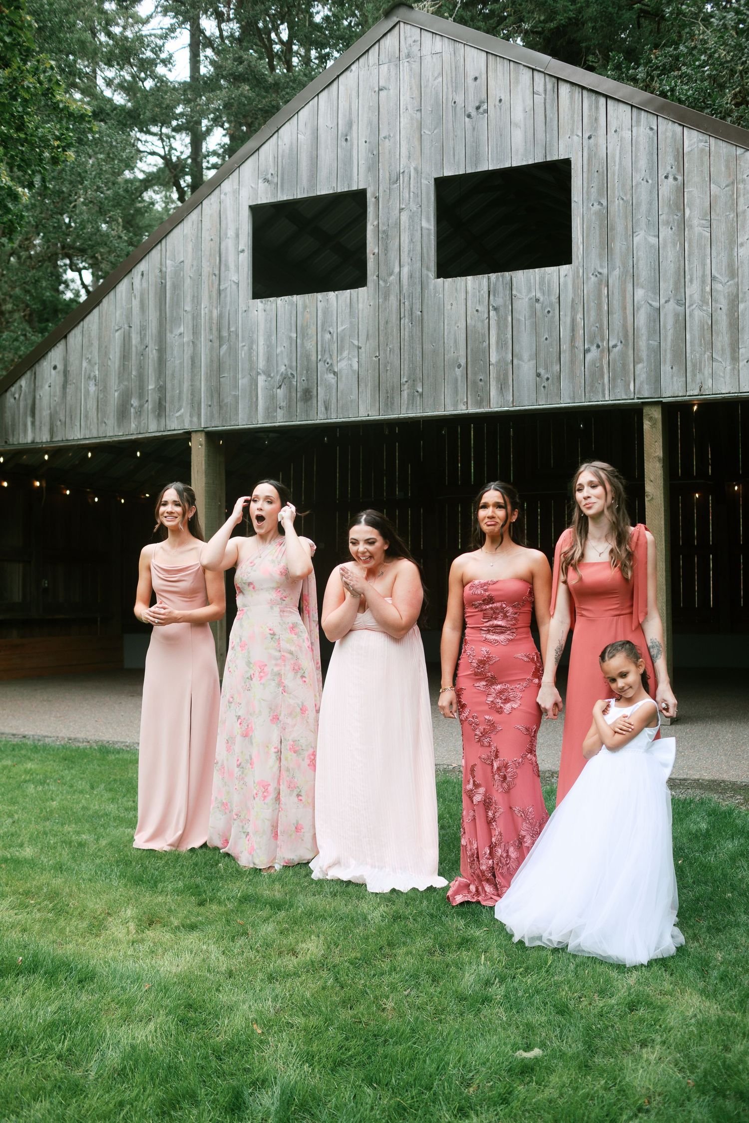 Wedding party in pink and coral dresses poses in front of a rustic wooden barn for wedding dress reveal - Adrianna Elizabeth photography.