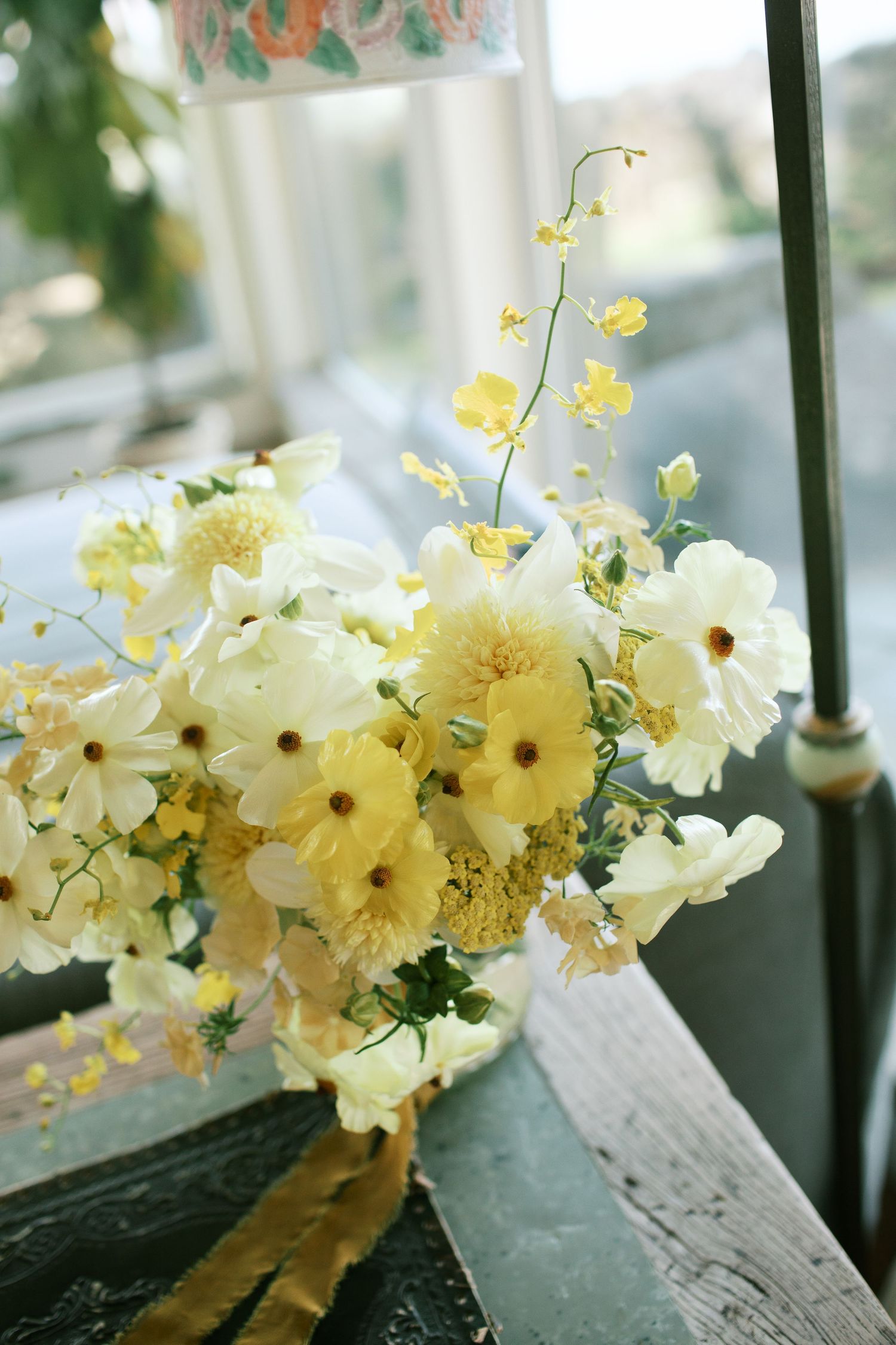 Delicate pale yellow orchids bloom in a cascading arrangement against a blurred background by a window.