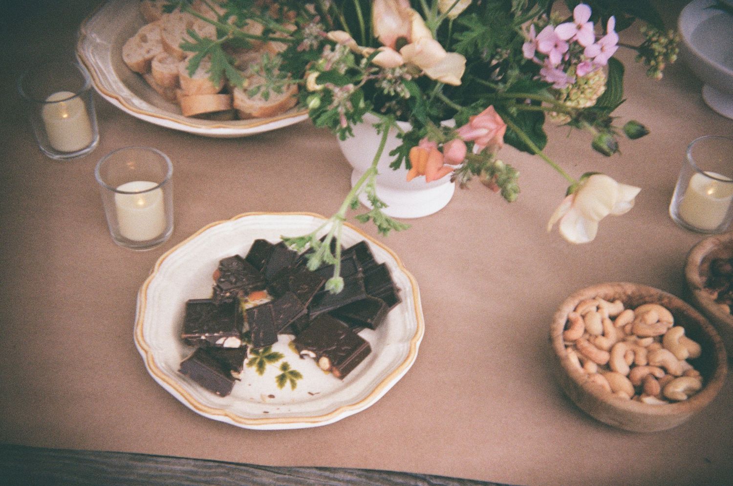 Elegant table setting with various plates of food and drinks arranged on a beige tablecloth in warm lighting.