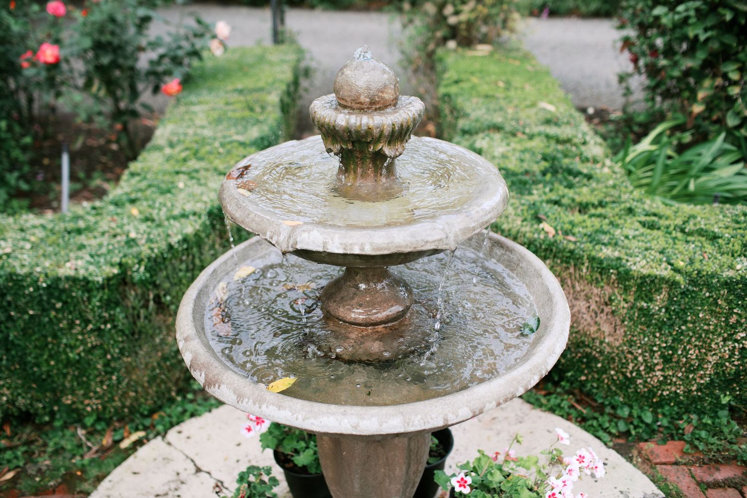 A stone tiered garden fountain with water cascading down multiple levels in a lush green garden setting.