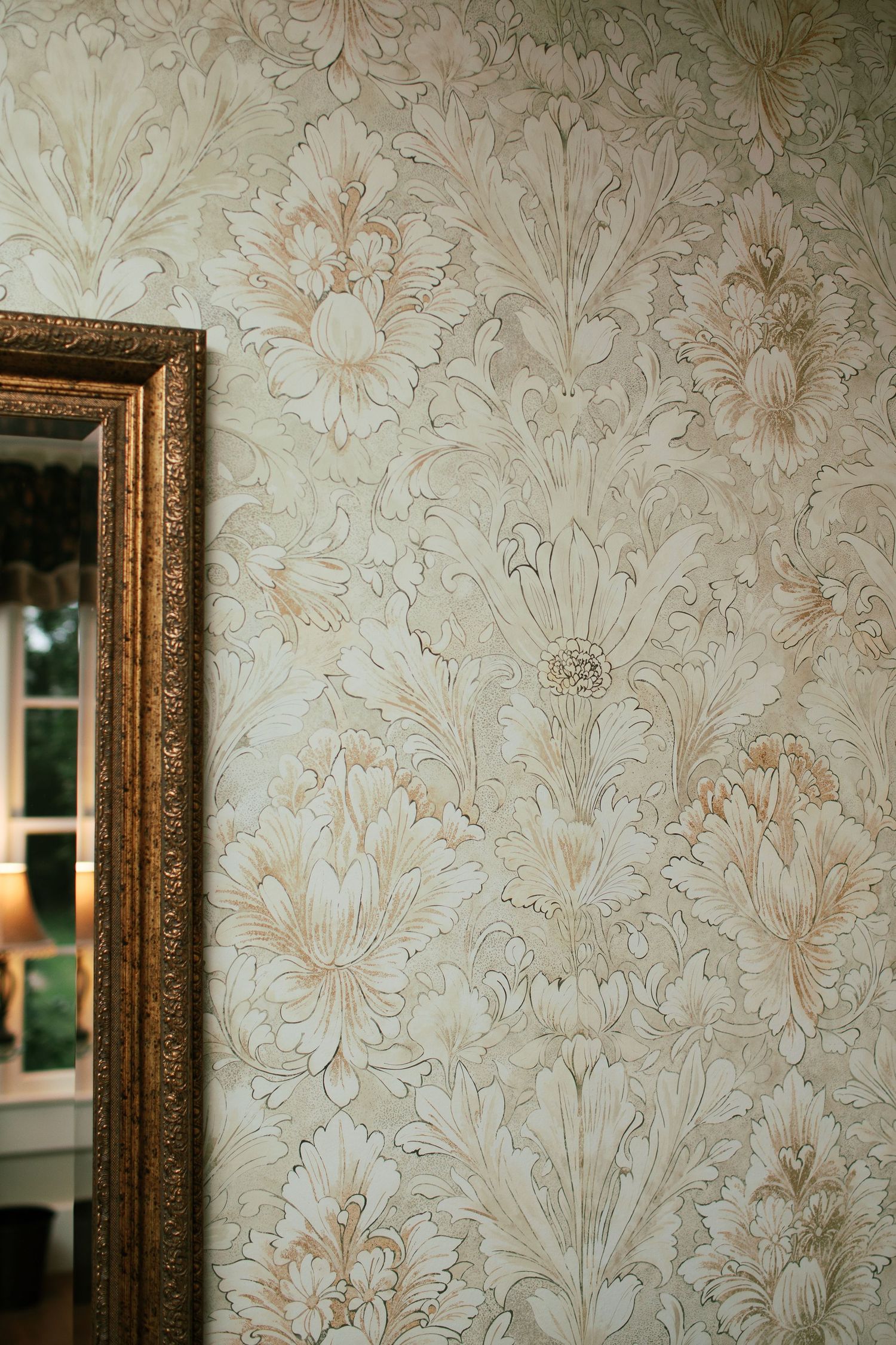 Vintage floral wallpaper pattern repeats across wall with ornate gold-framed mirrors mounted in a row.