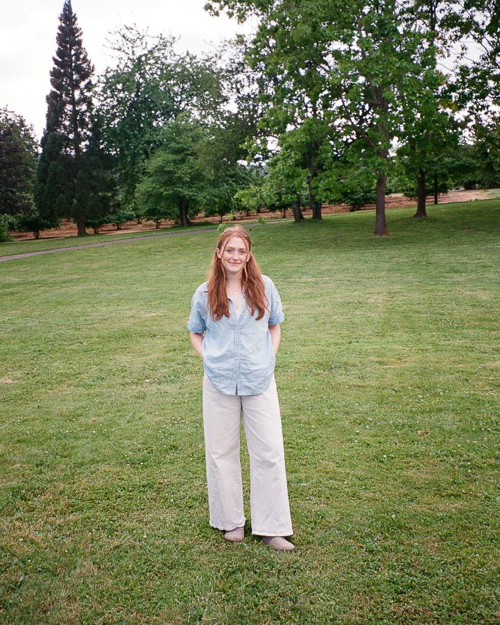 Adrianna Toohey stands in a grassy field wearing a light-colored outfit on a summer day on 35mm film-Adrianna Elizabeth Photography.