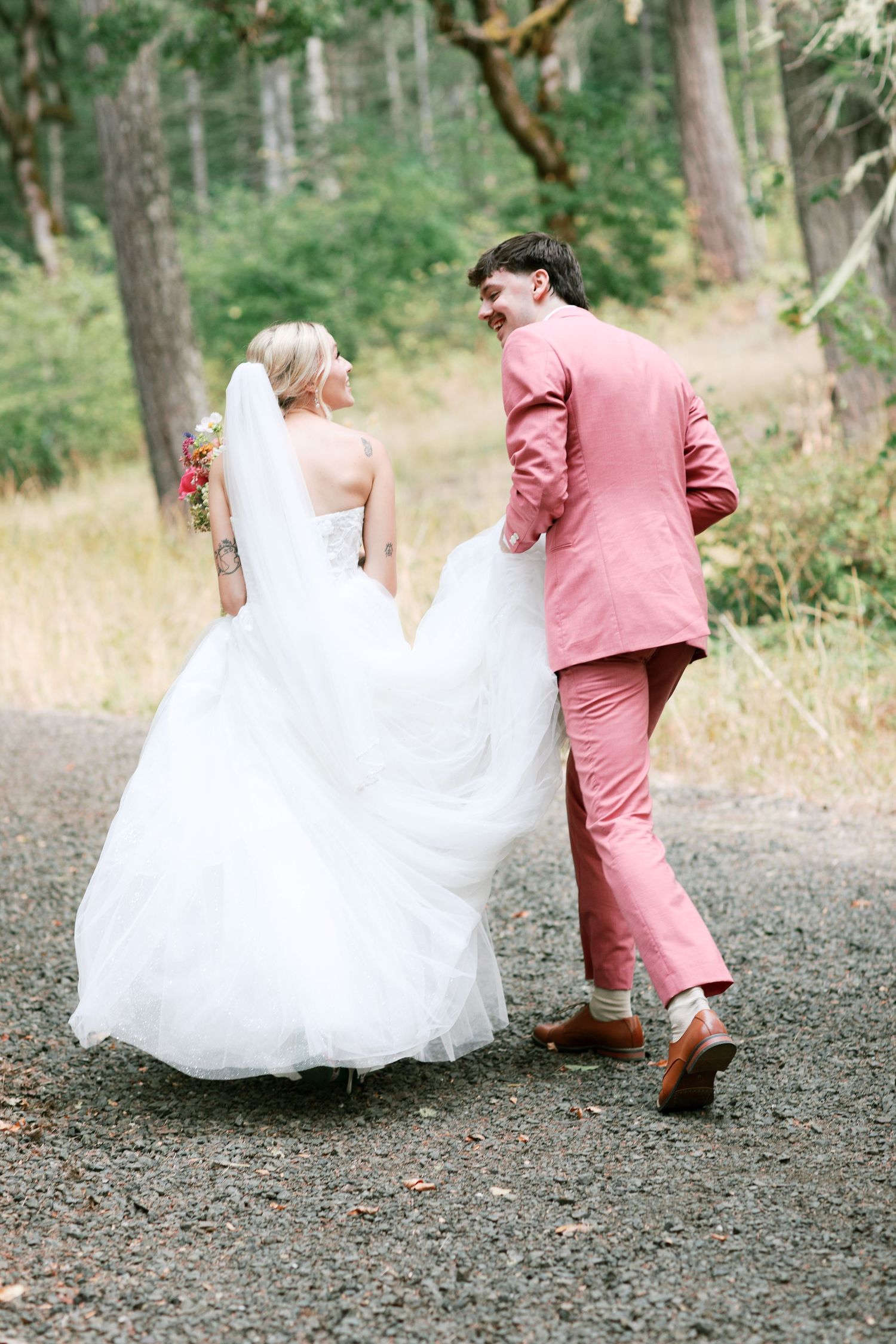 Joyful bride and groom walk together on a gravel path surrounded by nature - Adrianna Elizabeth Photography.