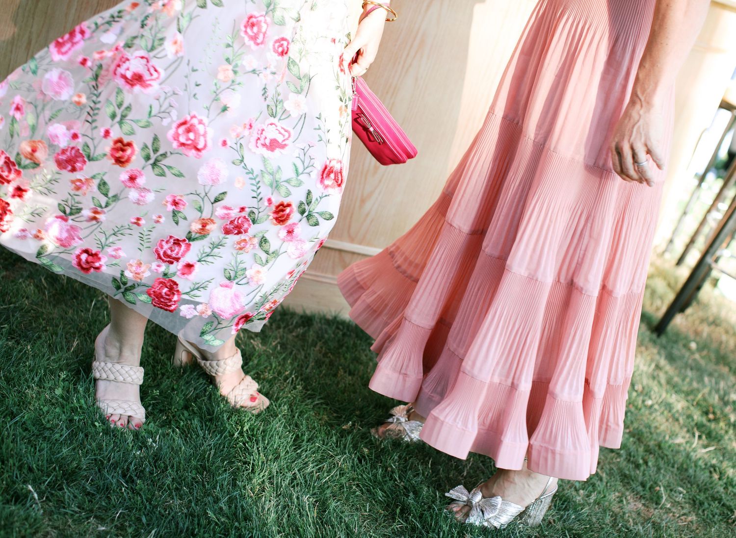Two flowy dresses in pink tones sway on grass, one with floral print and one solid, showing delicate lace trim details.