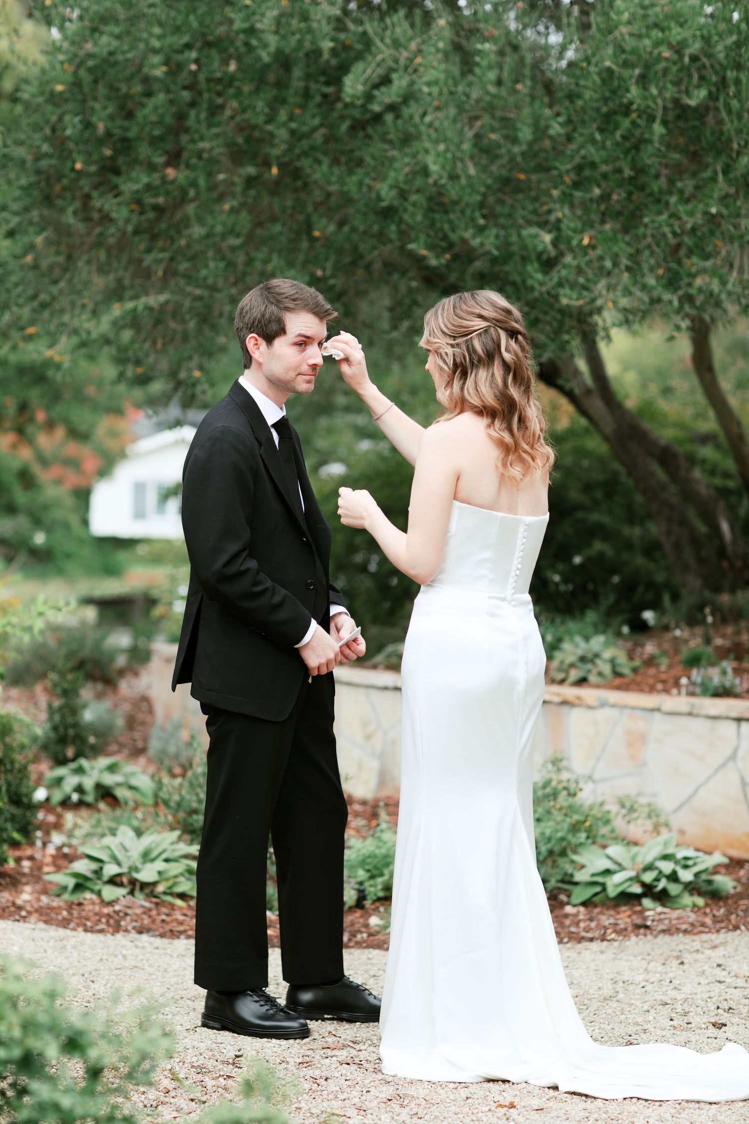 A couple in formal wedding attire share an intimate moment in a garden setting surrounded by greenery.