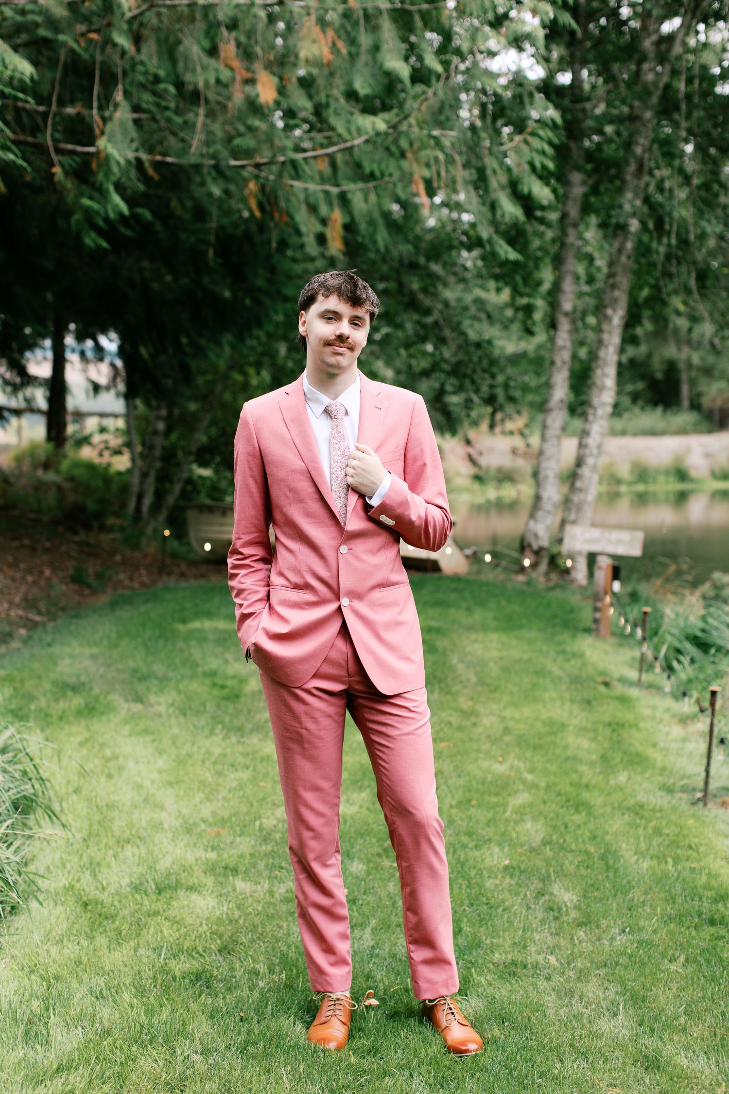 Groom wearing coral pink suit poses playfully on green lawn on 35mm film - Adrianna Elizabeth Photography.