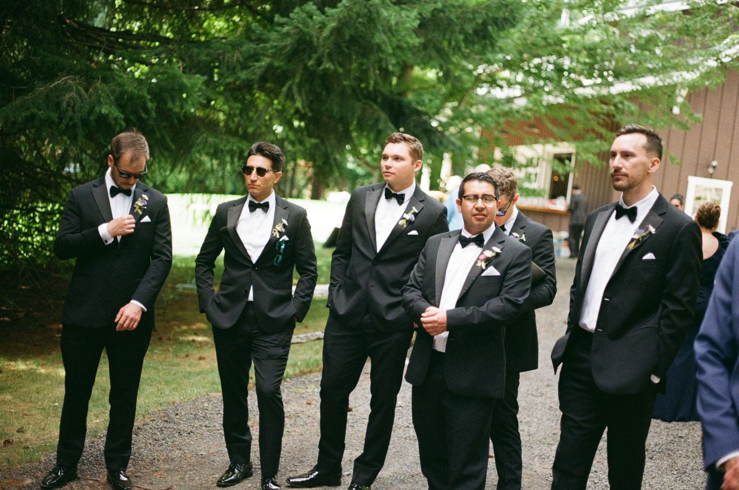 A group of groomsmen in black tuxedos walk together outdoors in a casual moment before the wedding ceremony on 35mm film.