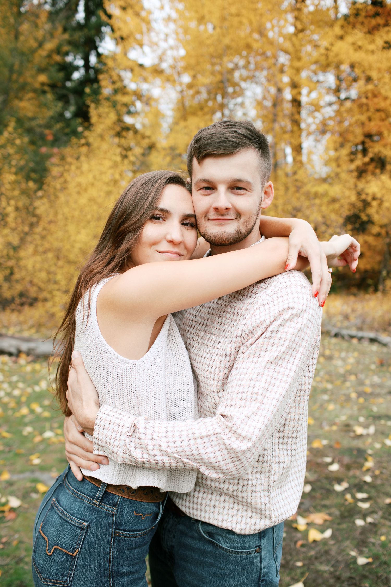 Couple embraces outdoors with golden autumn foliage in background during fall photoshoot.