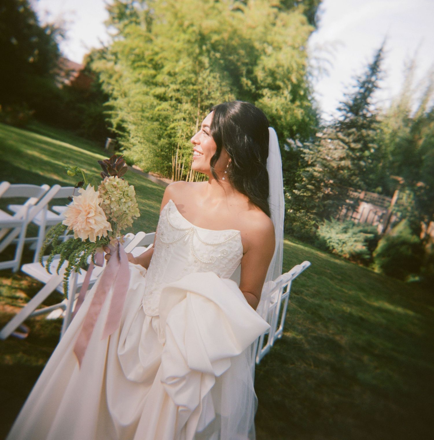 A flowing white wedding dress with a large bow detail captured in a sunlit garden setting.