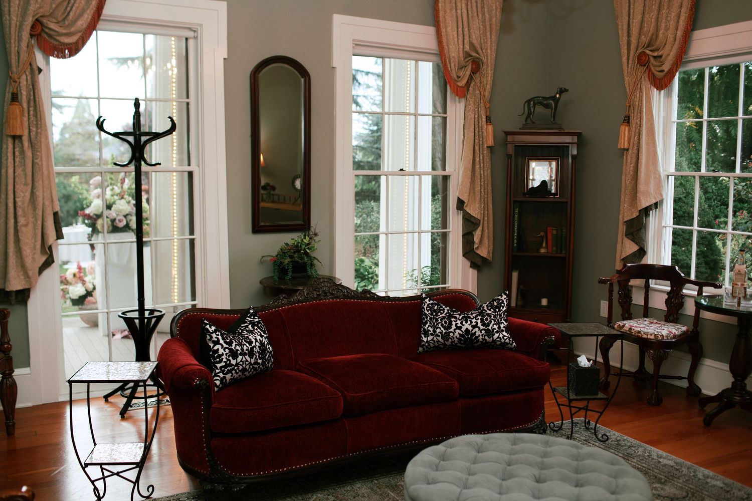 Elegant living room interior with burgundy sofa, tall windows, hardwood floors, and classic drapery treatments.