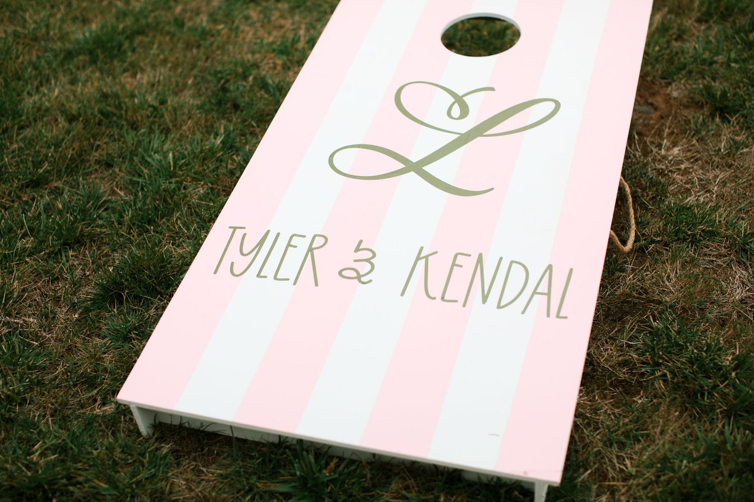 White cornhole boards with monogram designs sit on grass during an outdoor event setup.