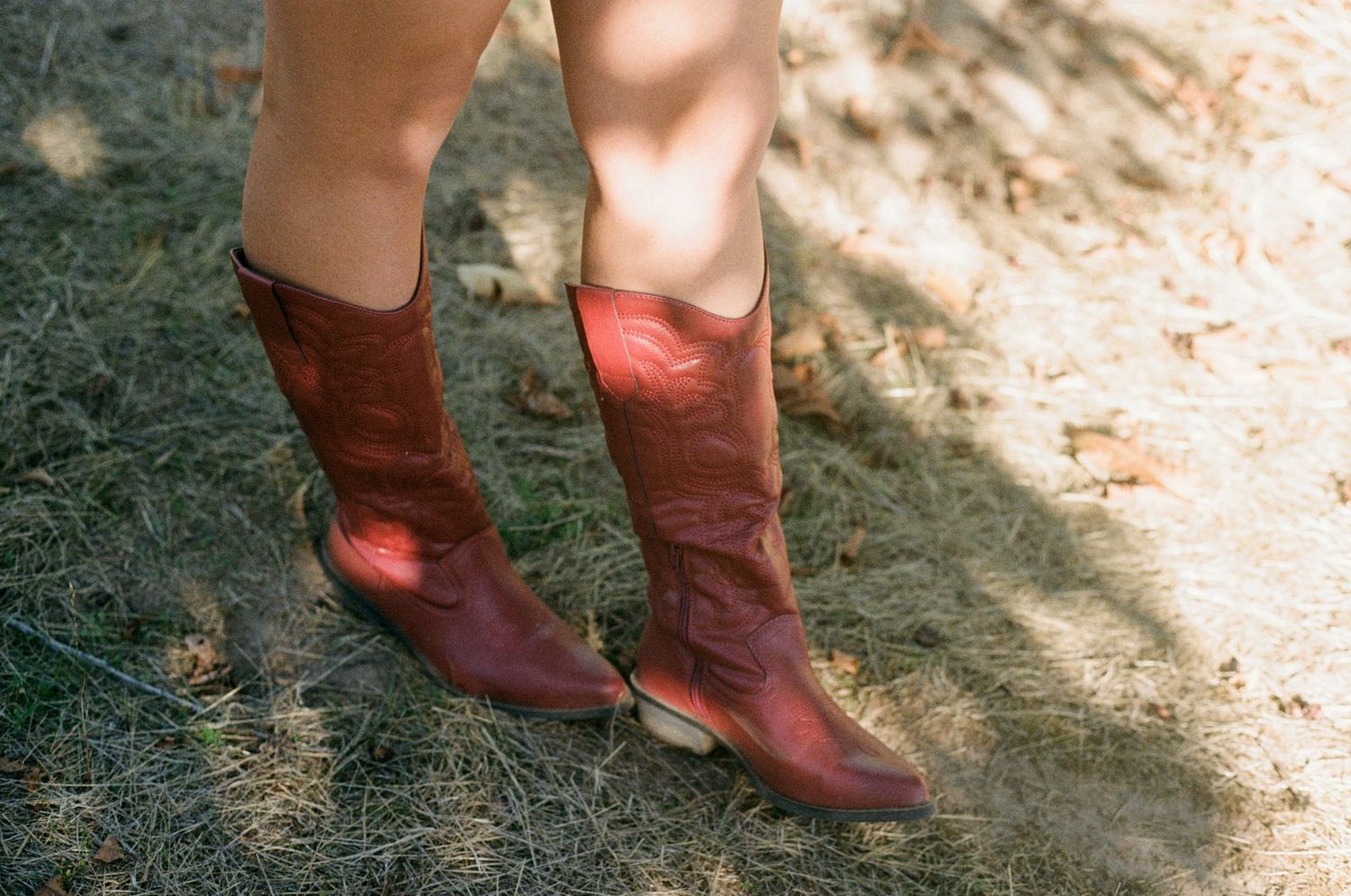 Senior session in red cowgirl boots stand beside a rustic woven basket on dry ground on 35mm film-Adrianna Elizabeth Photography.