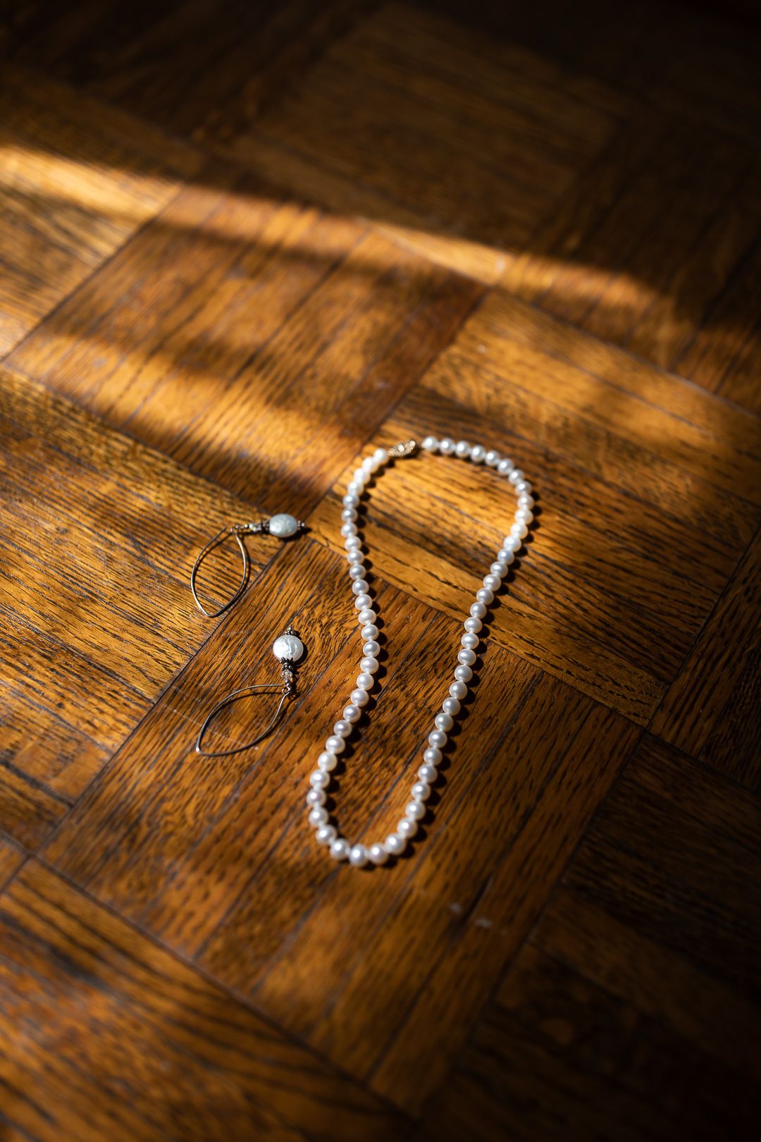 White pearl necklace arranged in a curved line on a rustic wooden surface with dramatic lighting.