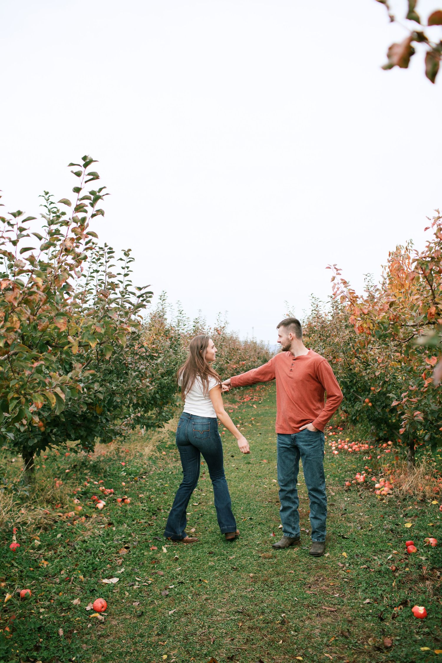 People enjoying a fall day at an apple orchard with rows of trees displaying autumn colors in the background.