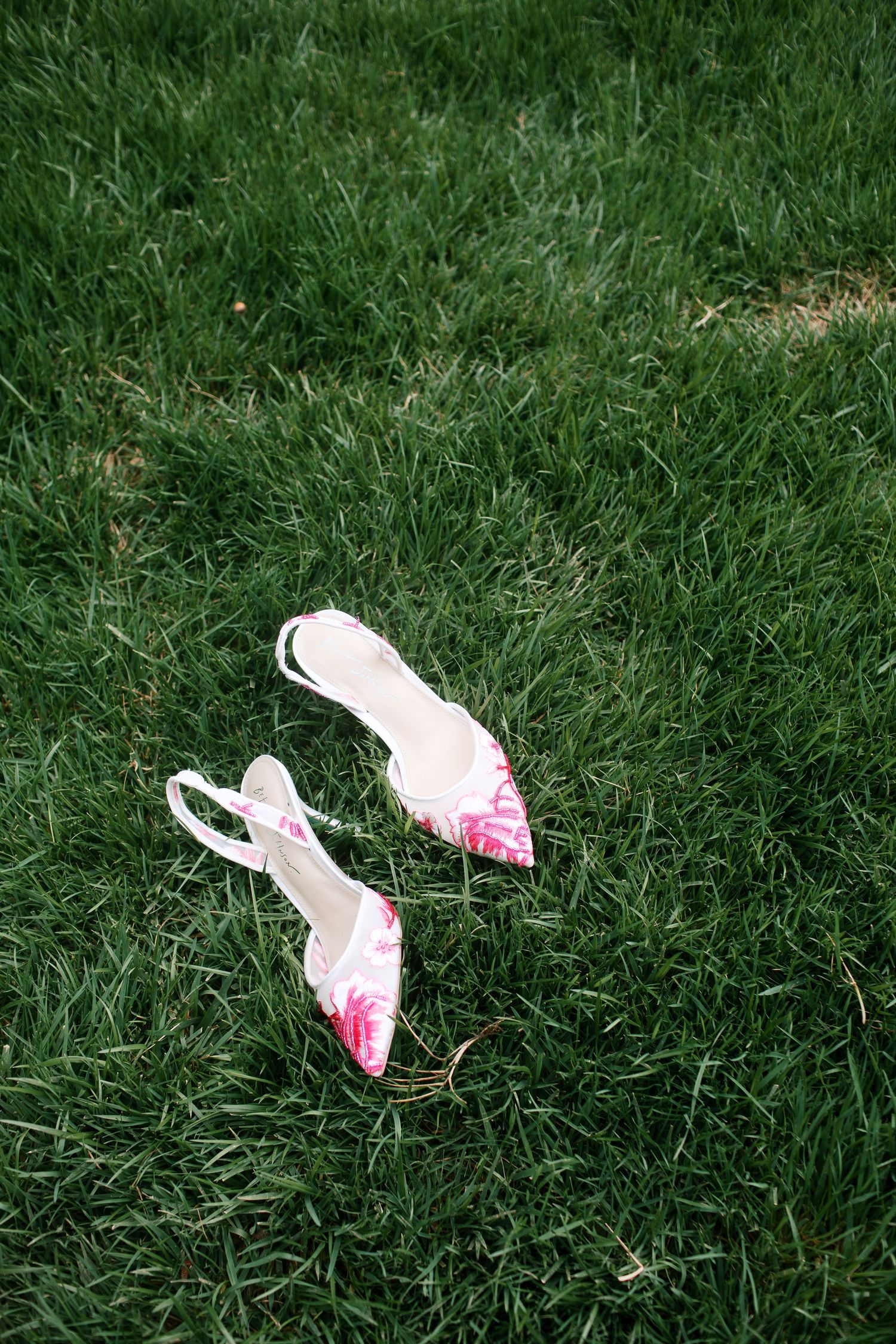 Betsy Johnson pink embroidered bridal shoes placed on lush green grass - Adrianna Elizabeth Photography.