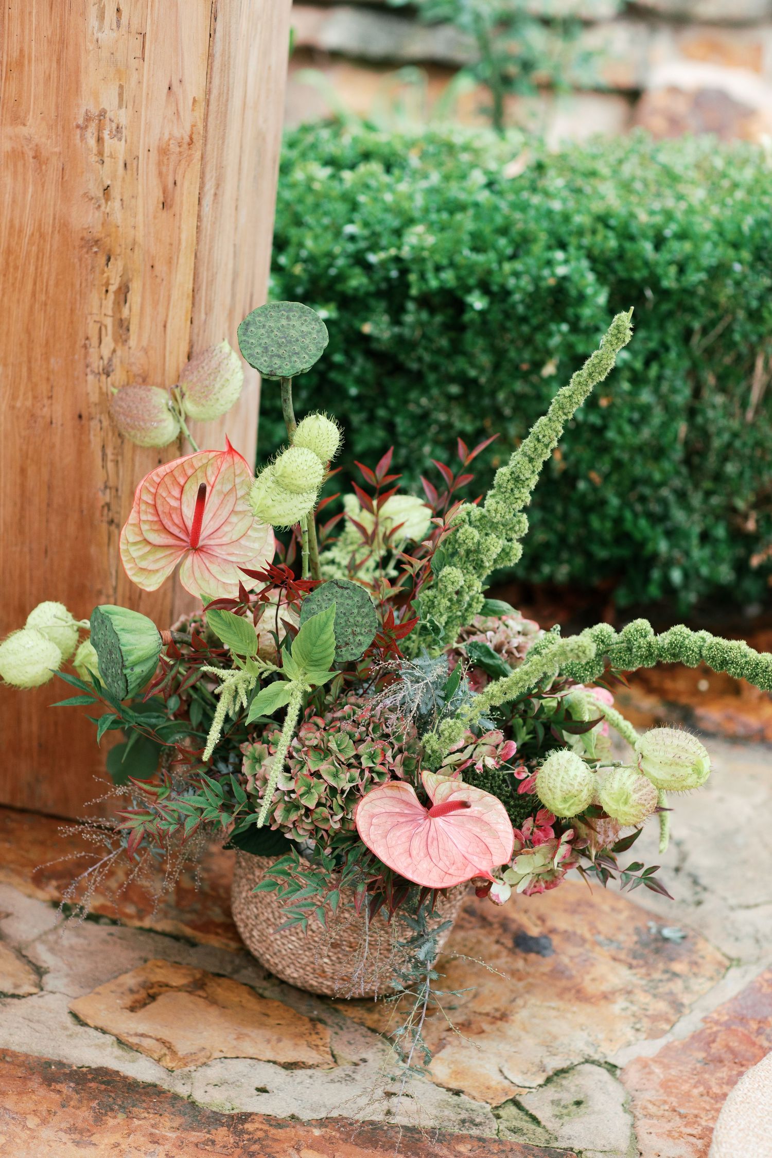 Pink anthurium flowers and green foliage arranged in a rustic wooden container on a textured stone surface.
