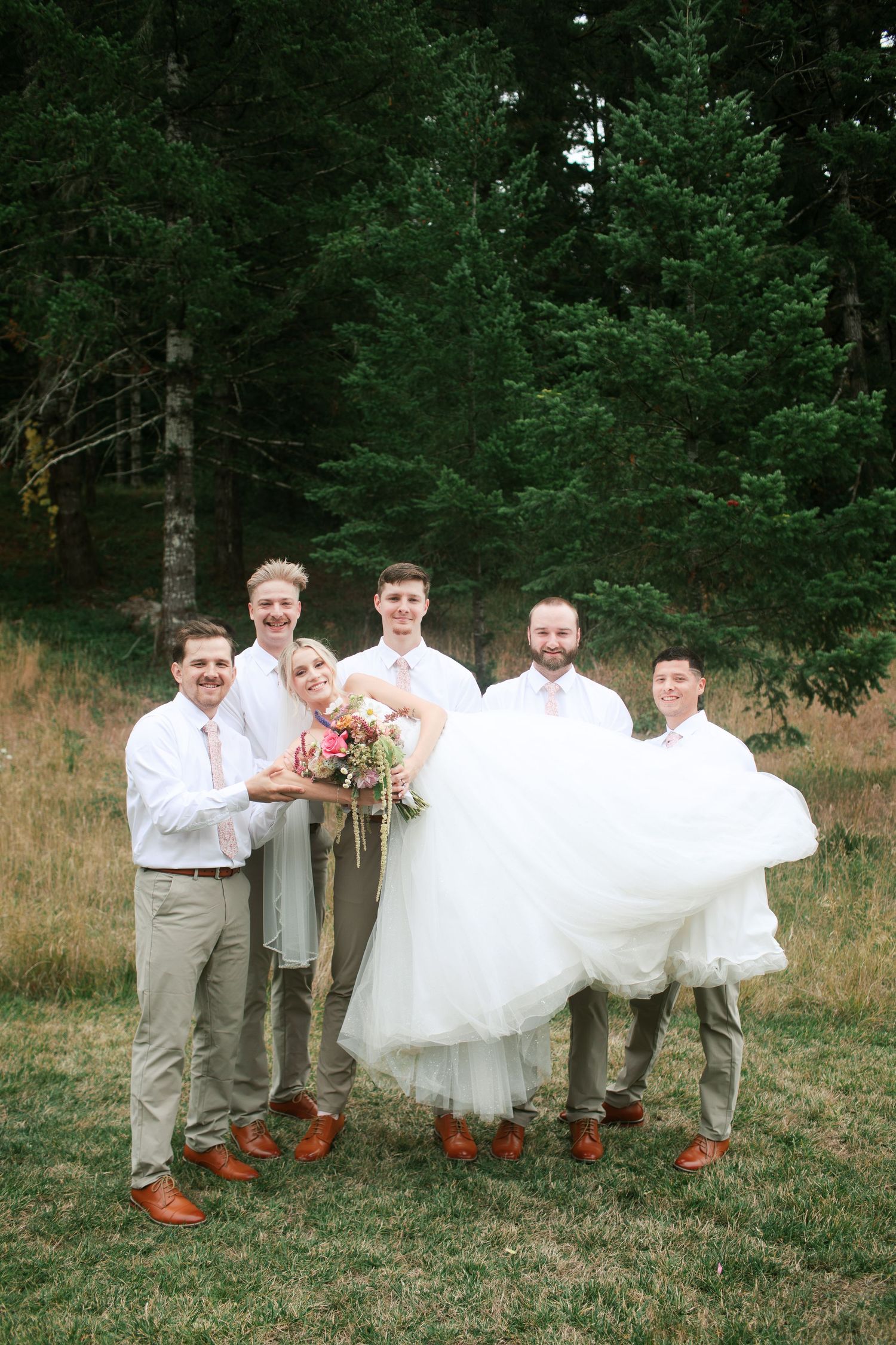 Playful wedding party photo with groomsmen lifting bride in white dress outdoors-Adrianna Elizabeth Photography.