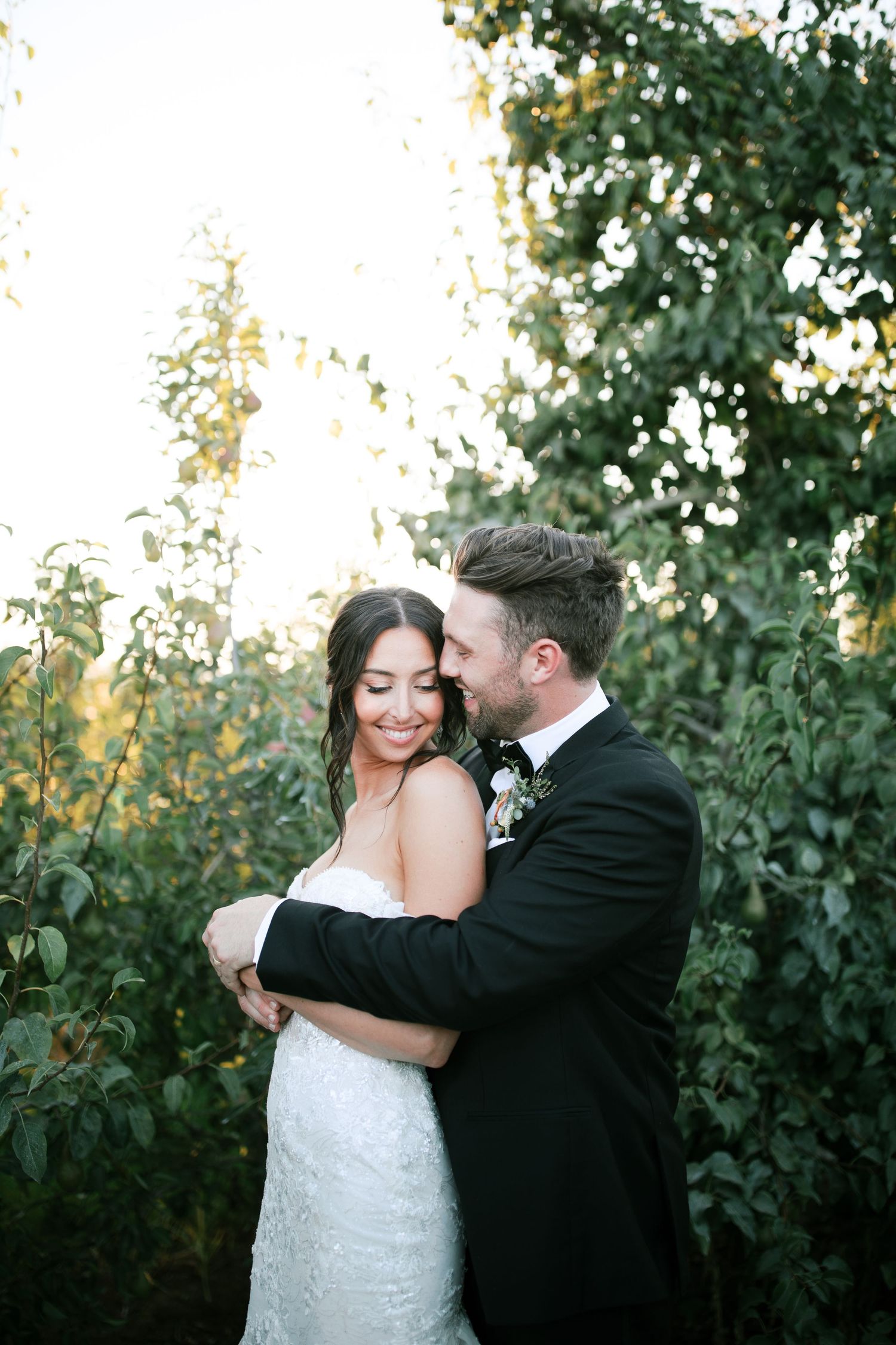 A romantic wedding couple shares an intimate moment outdoors surrounded by lush greenery at sunset.