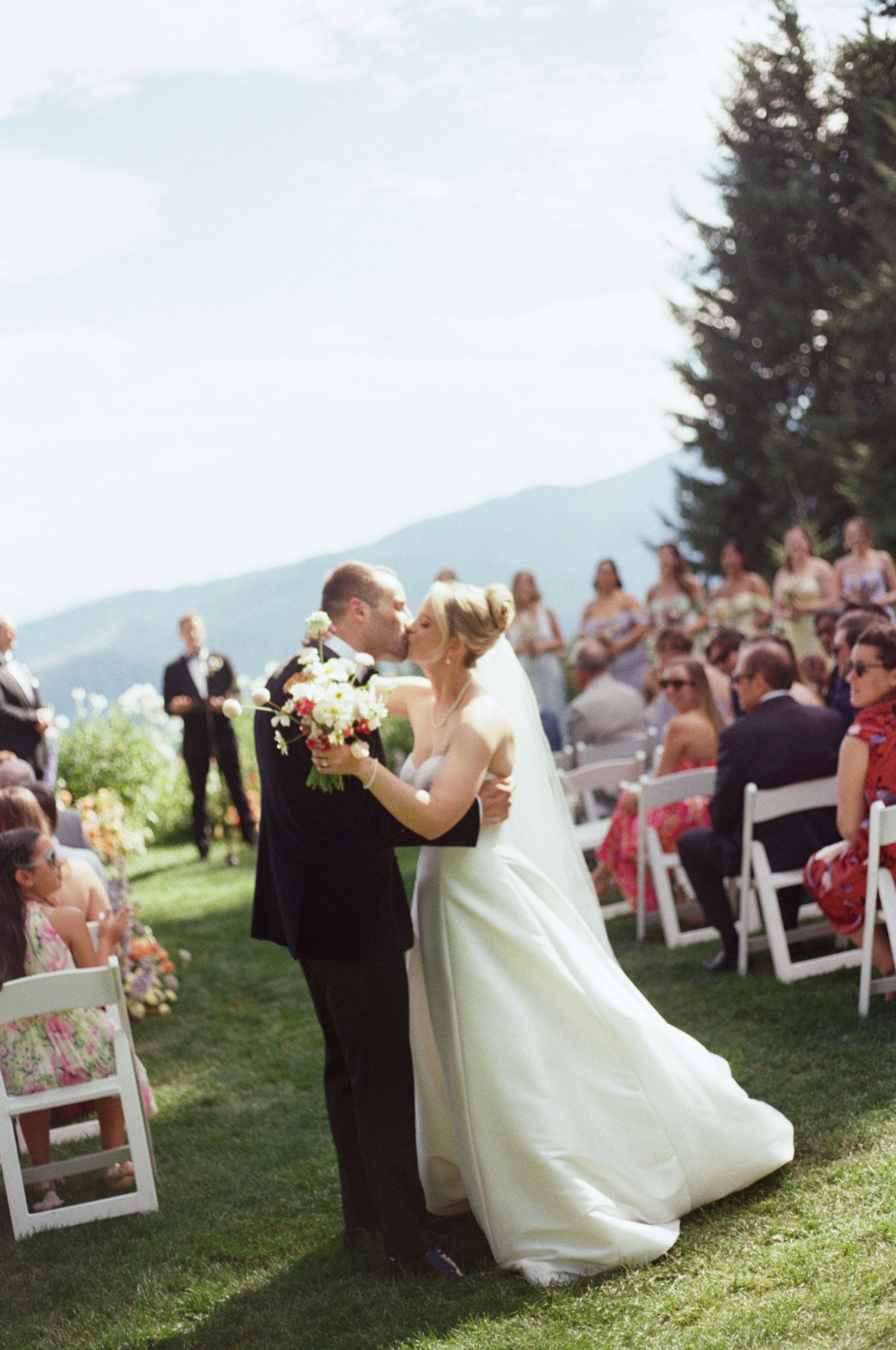 A romantic first dance at an outdoor mountain wedding with guests seated on white chairs in the background.