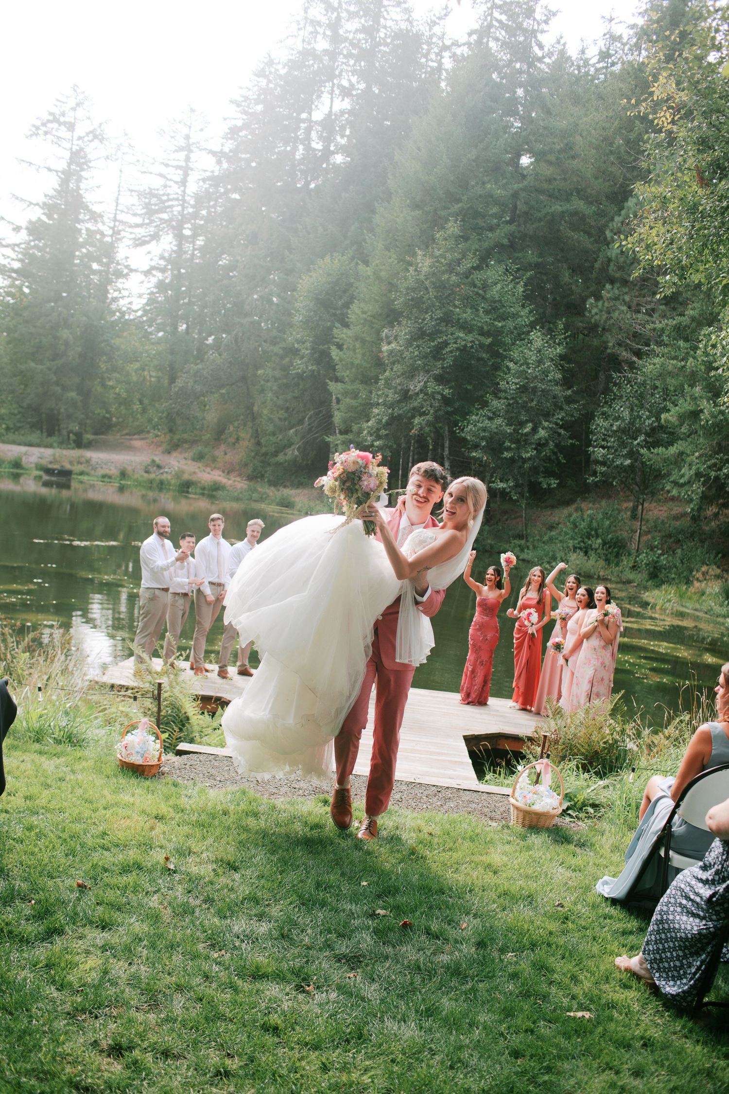 Groom carrying bride after ceremony party on a grassy lawn with a lake in the background - Adrianna Elizabeth Photography.