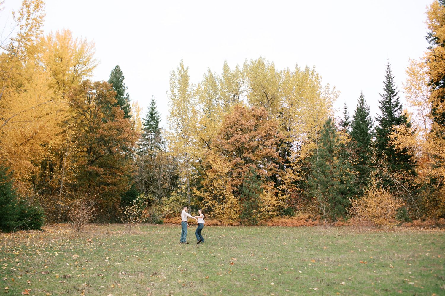 A couple walks together through a scenic autumn landscape with golden trees and fallen leaves on the ground.