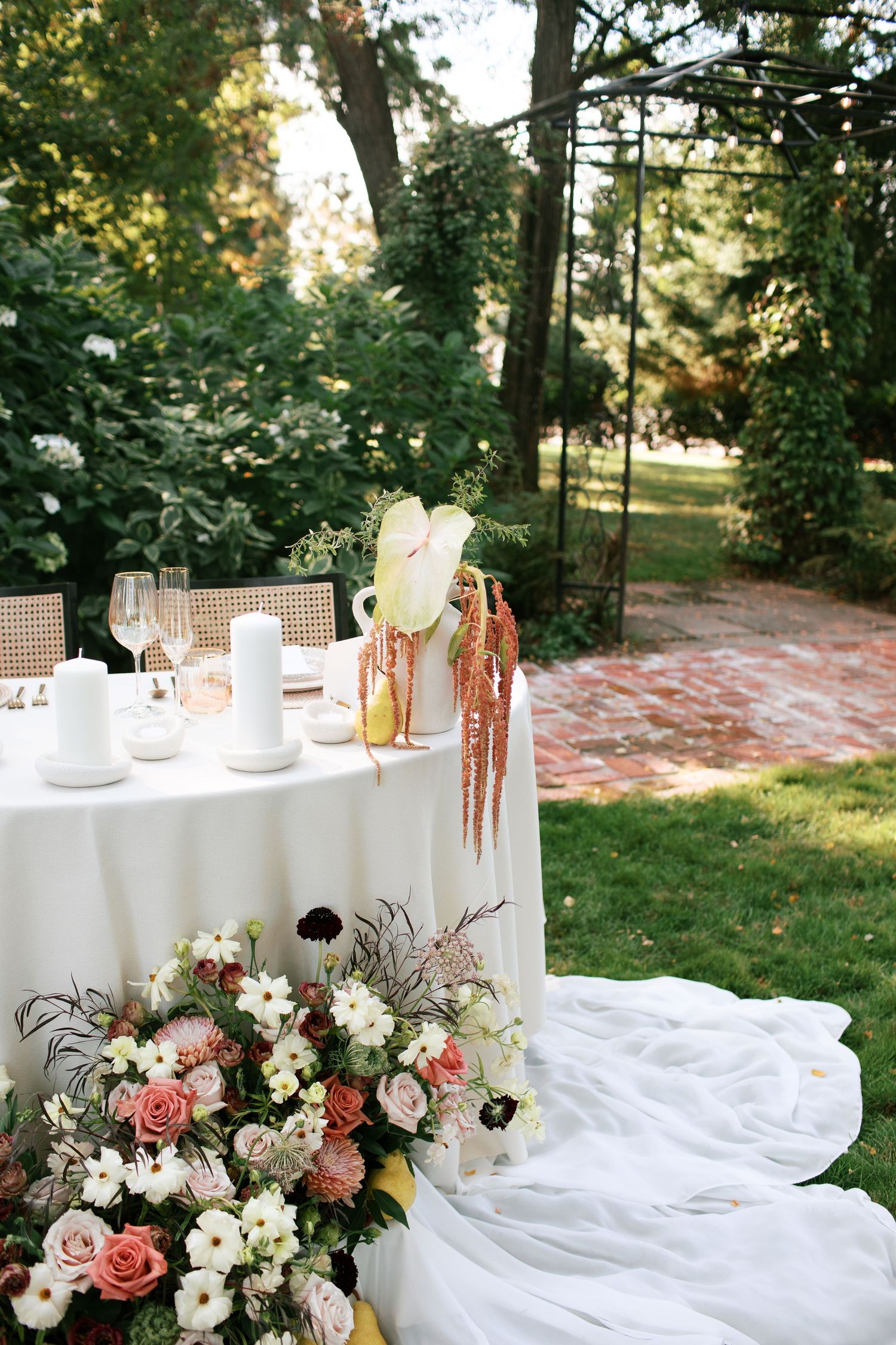 Elegant outdoor wedding table setup with flowing white linens and romantic pink and white floral arrangements in a garden setting.