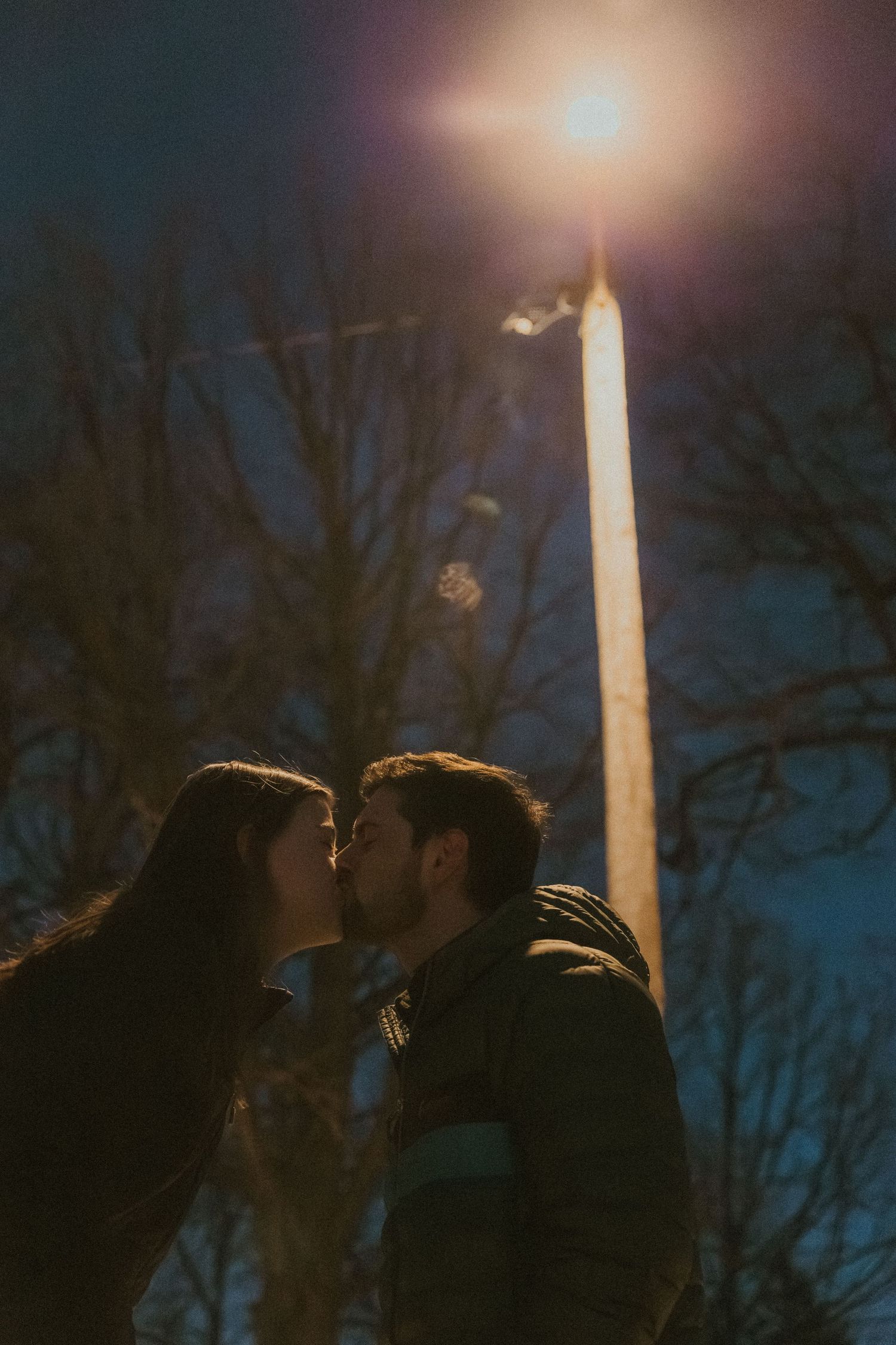couples shares a kiss under a street light during snowy couples session with central illinois photographer
