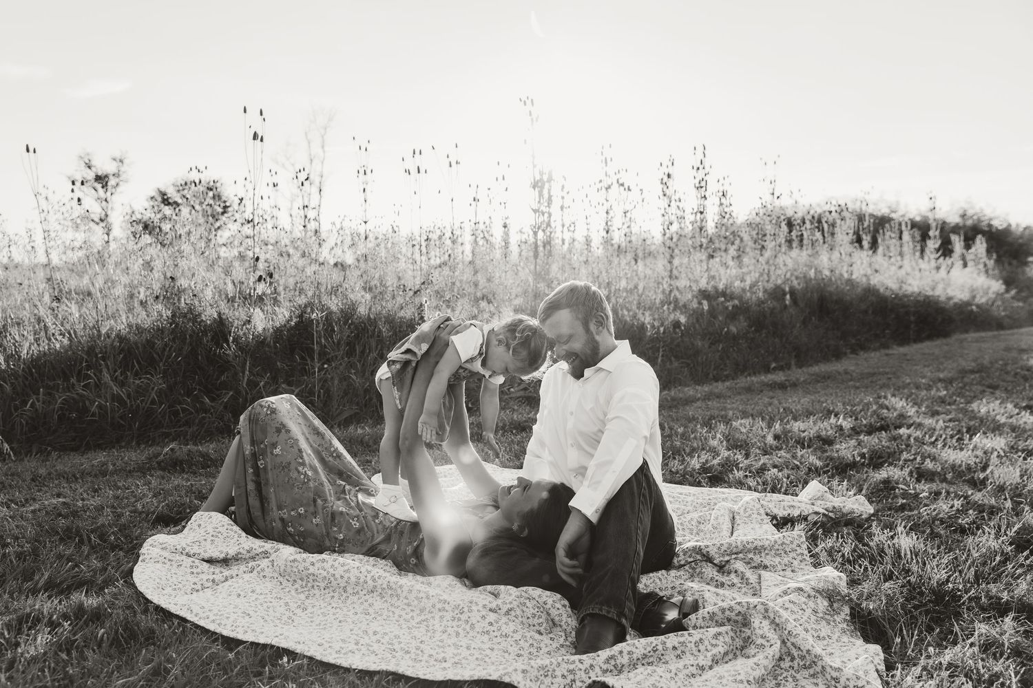 Family cuddles on a blanket in an open field during golden hour while doing airplanes with their daughter during a family session in IL