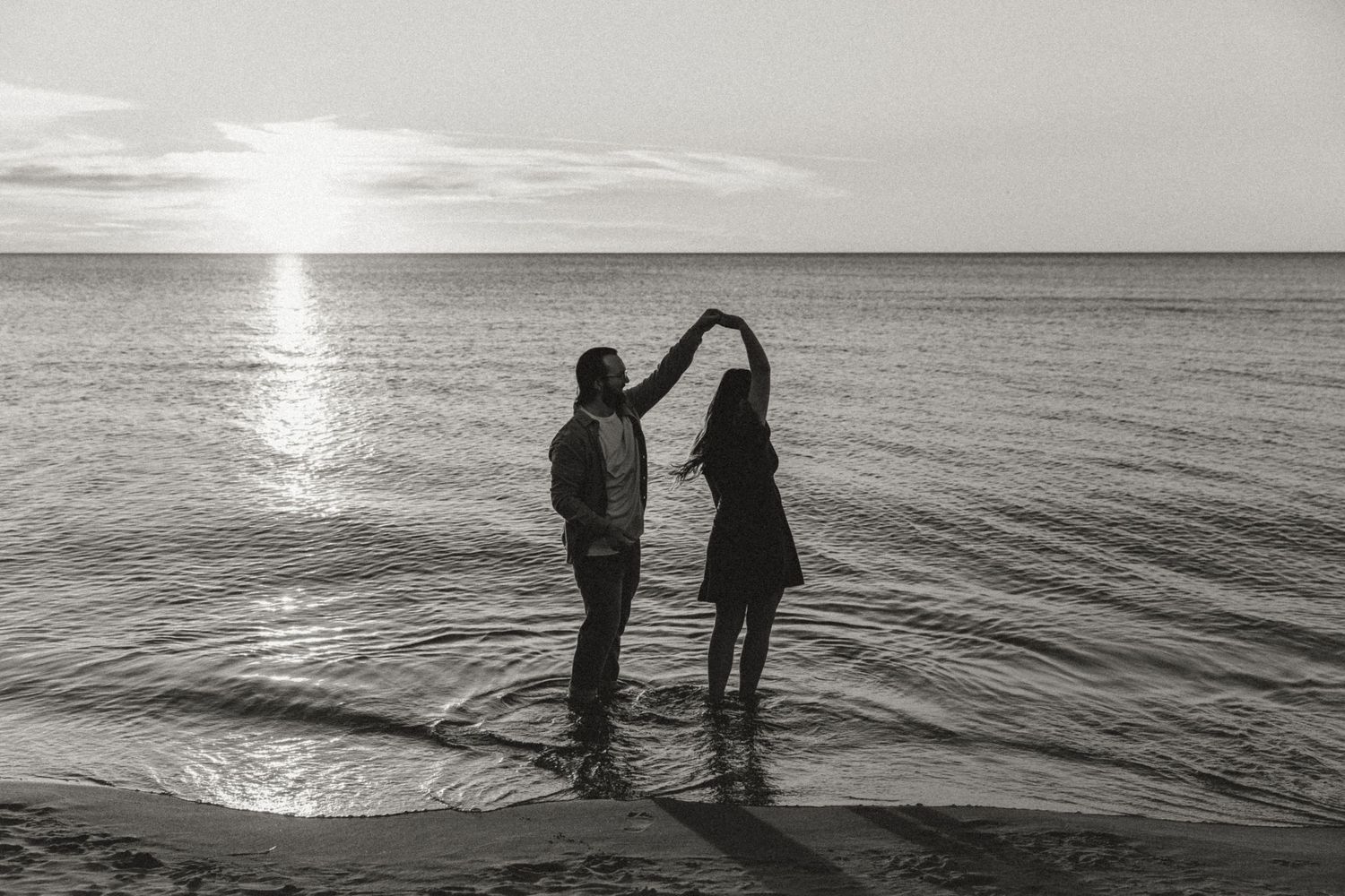 Future Groom spins future bride in lake michigan during their engagement session while illinois wedding photographer captures their love