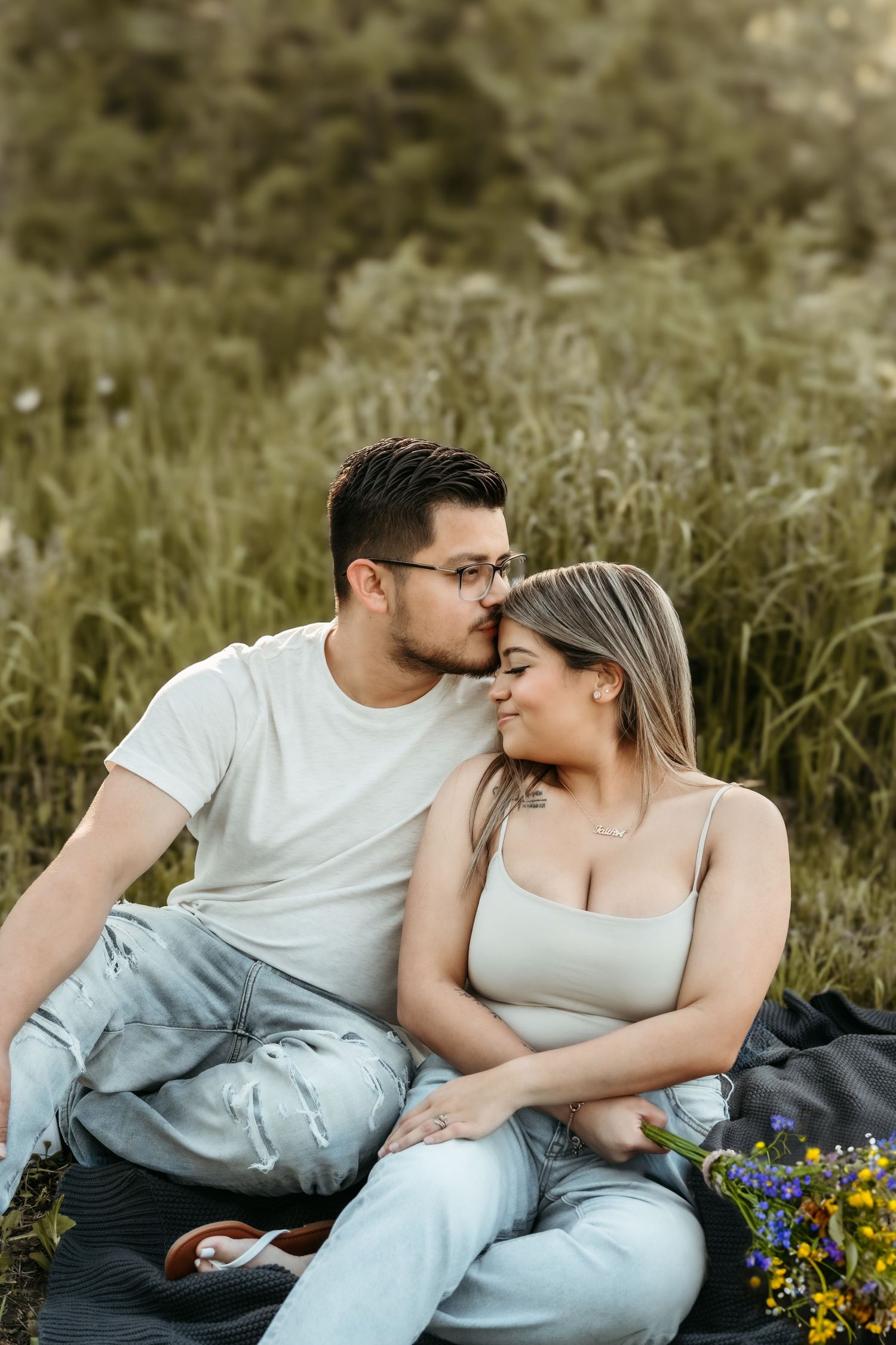 Couple sitting on the grass, with the guy kissing the girl's head