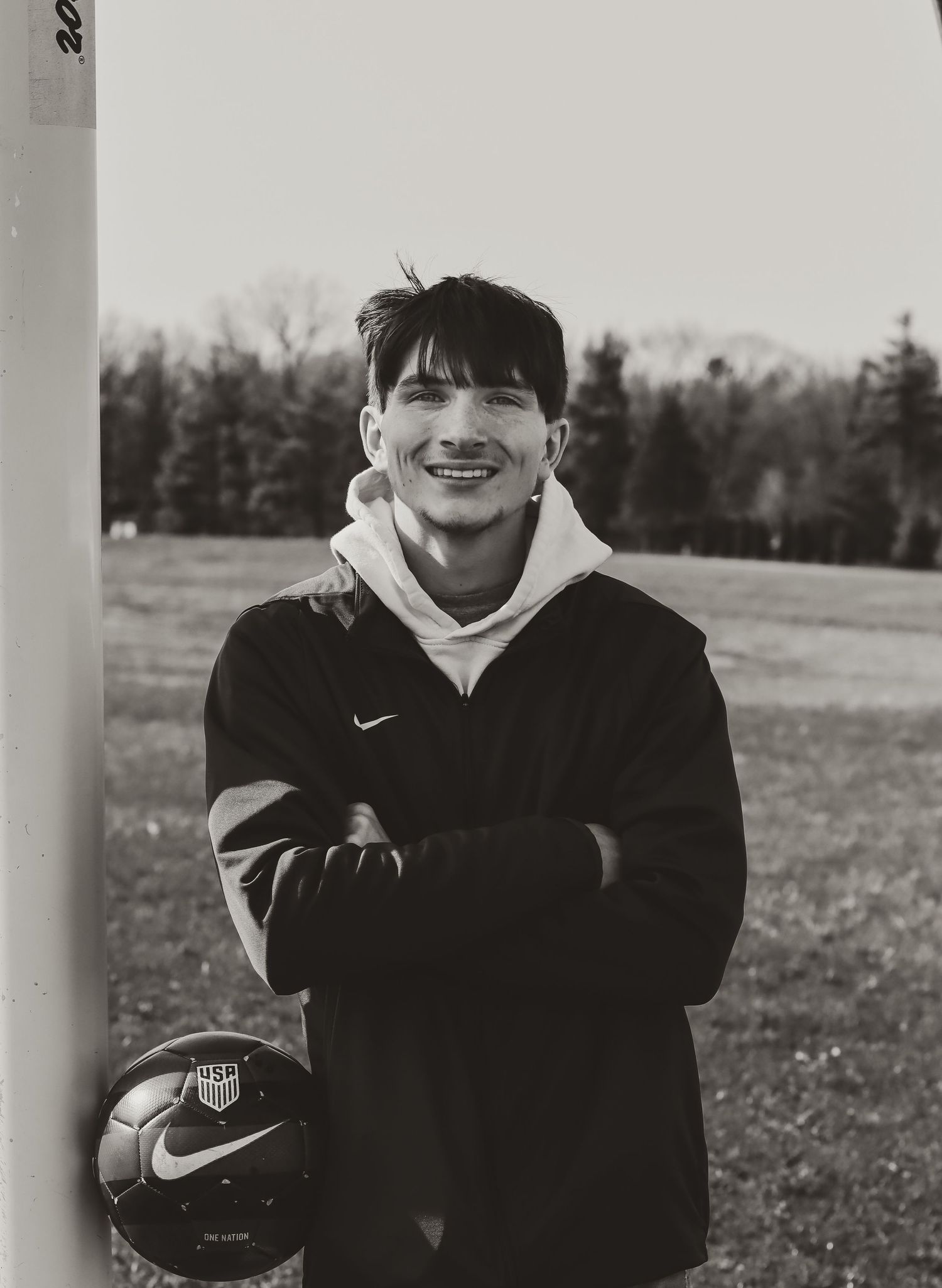 High school senior soccer athlete poses with soccer ball in his soccer field during a senior photo session