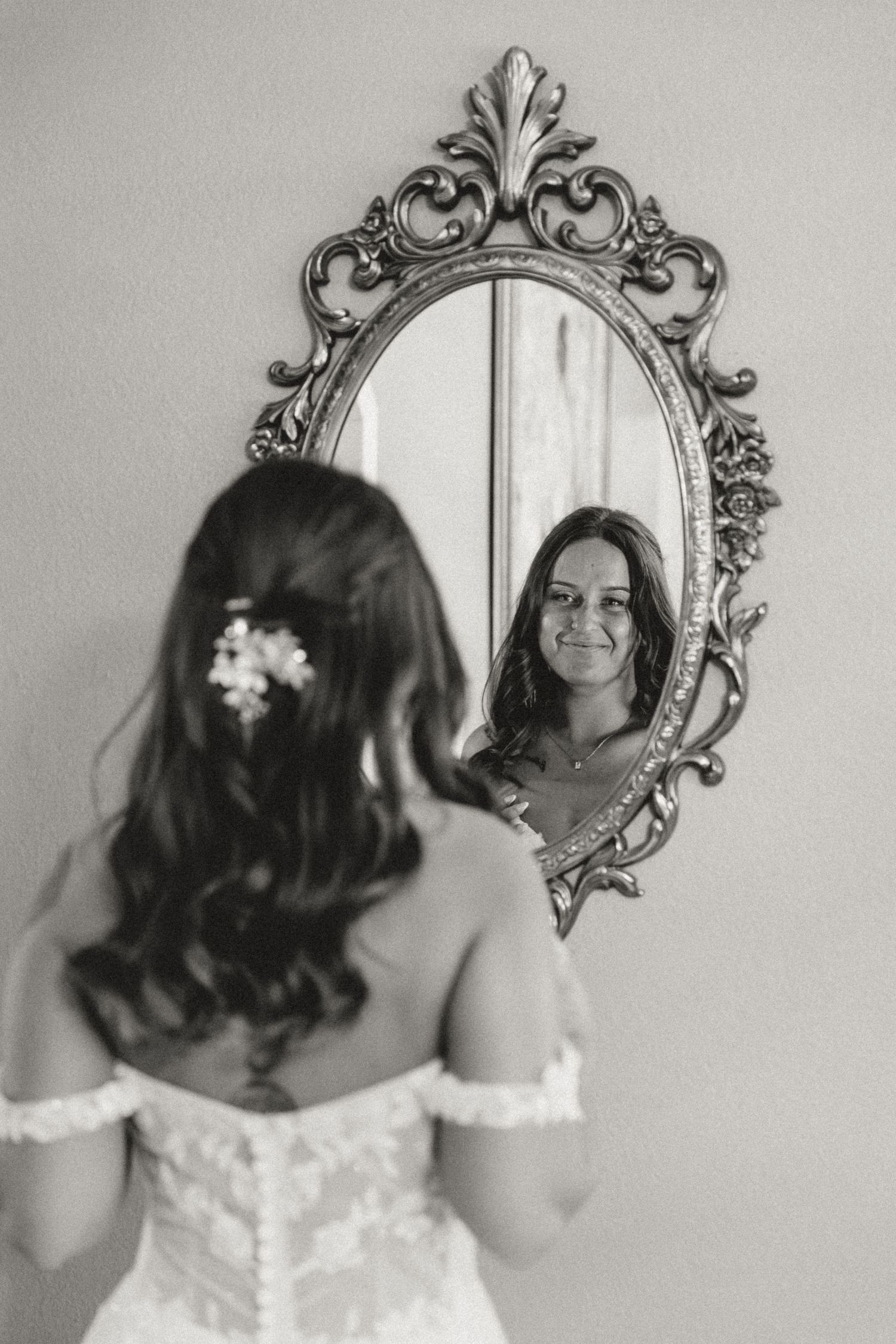 Bride takes in how she looks on her wedding day in front of gold vintage mirror while central il photographer captures the moment