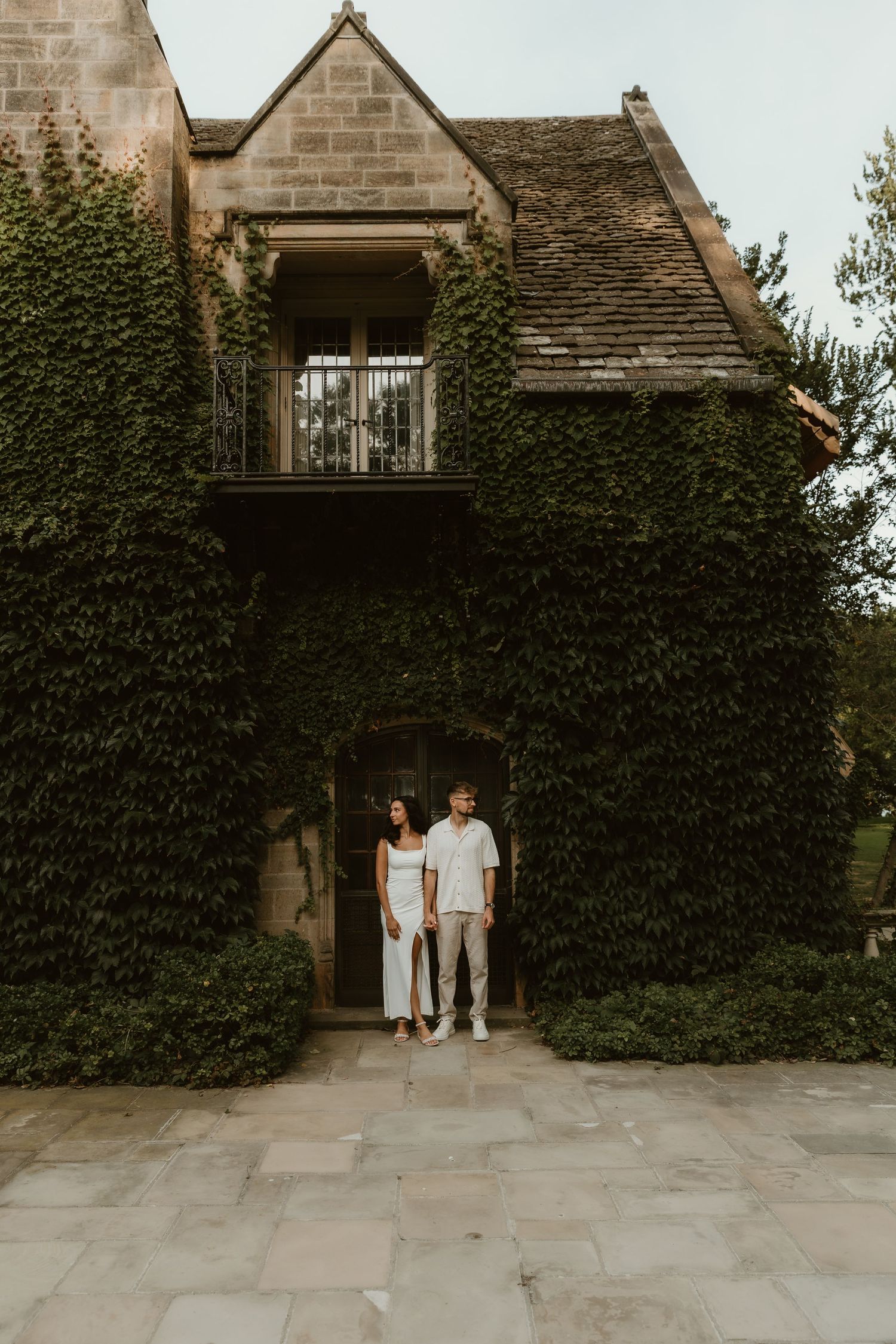 Couple holding hands in front of ivy-covered stone building. Serene, romantic scene with historic architecture