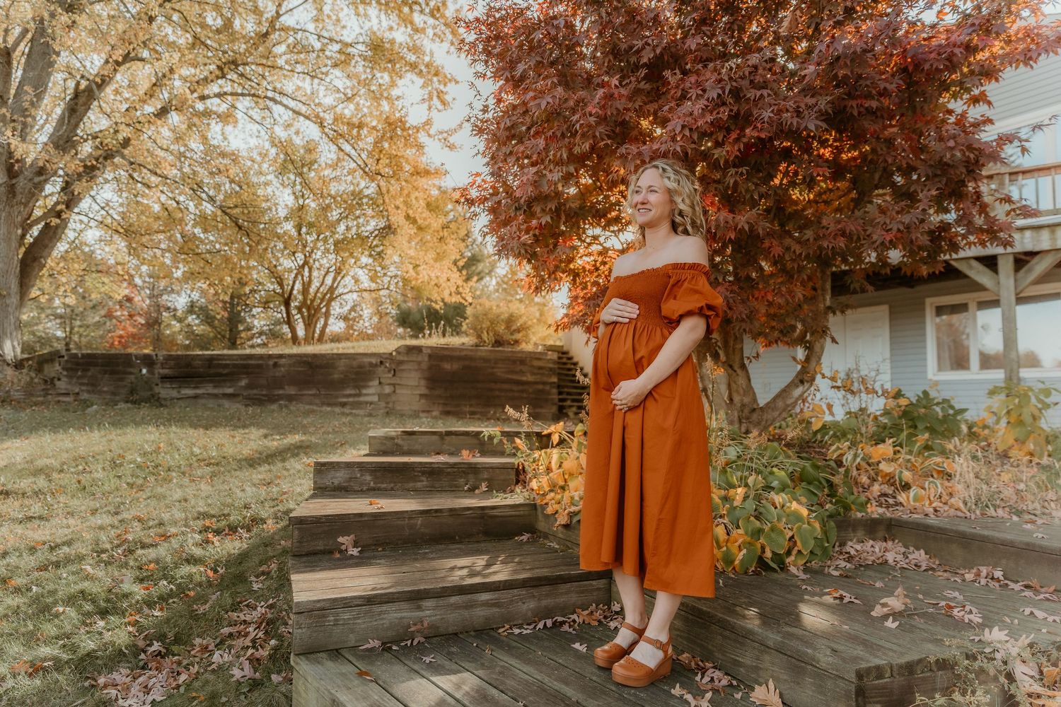 Expecting mom holds her belly and gazing out into nature during a beautiful sunrise with central il maternity photographer