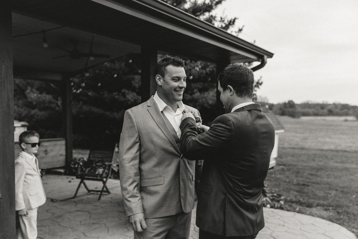 Best man helps groom put on his boutonniere during getting ready moments before wedding ceremony
