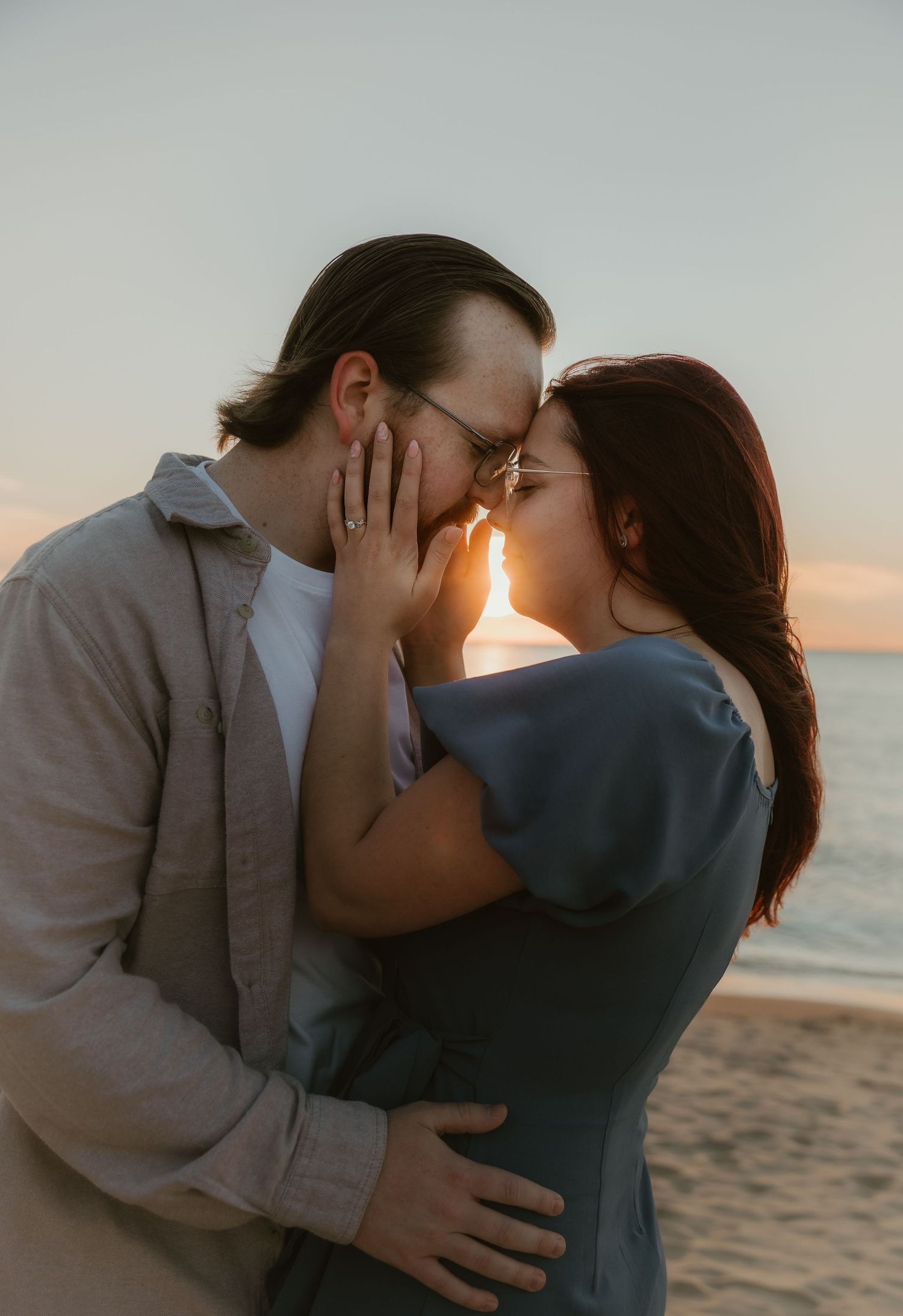 Romantic sunset beach engagement photo of a couple, gently touching foreheads bathed in golden light. highlighting emotional connection