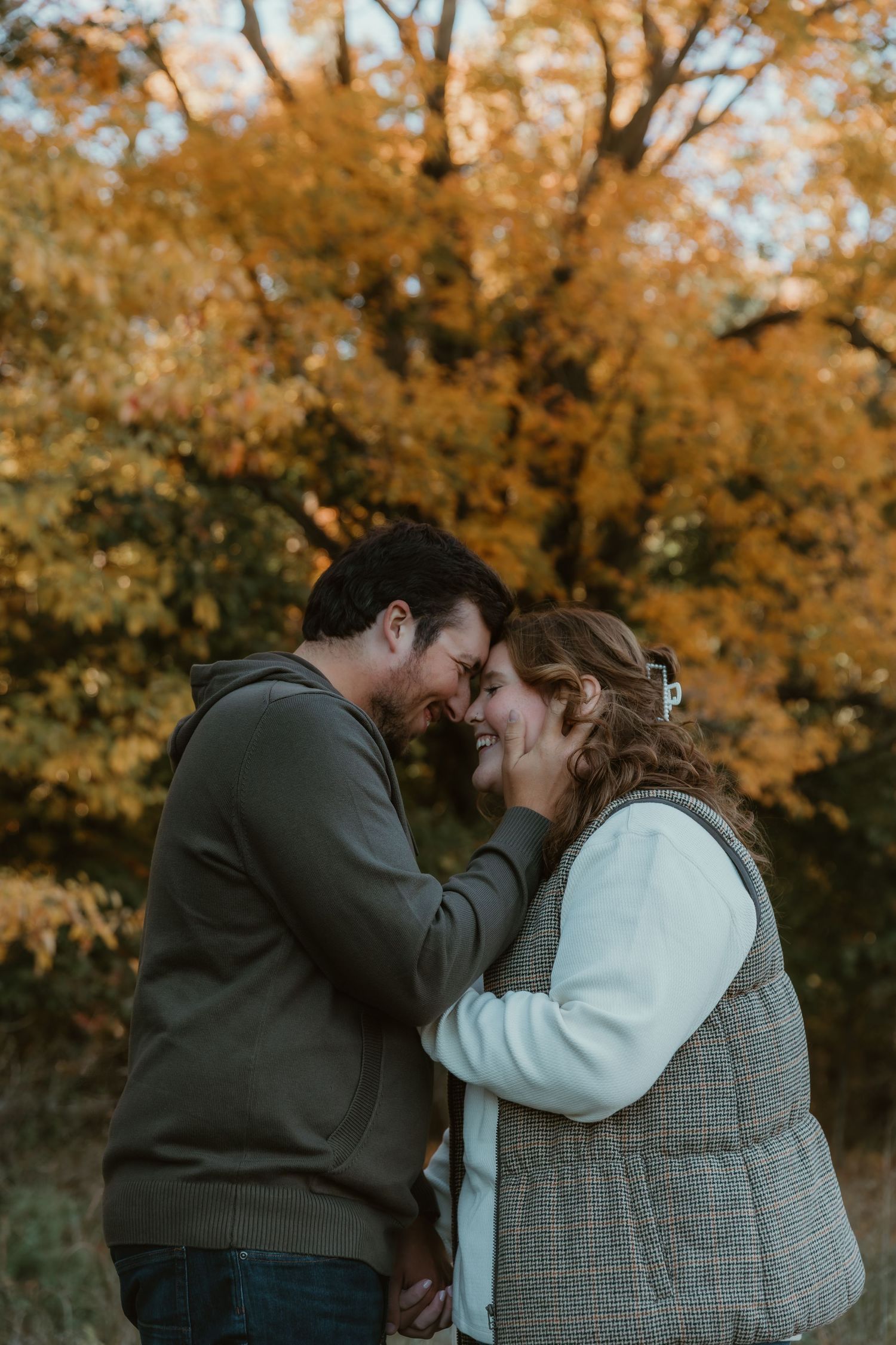 Couple embraces each other for a hug in front of a fall tree for their engagement photos