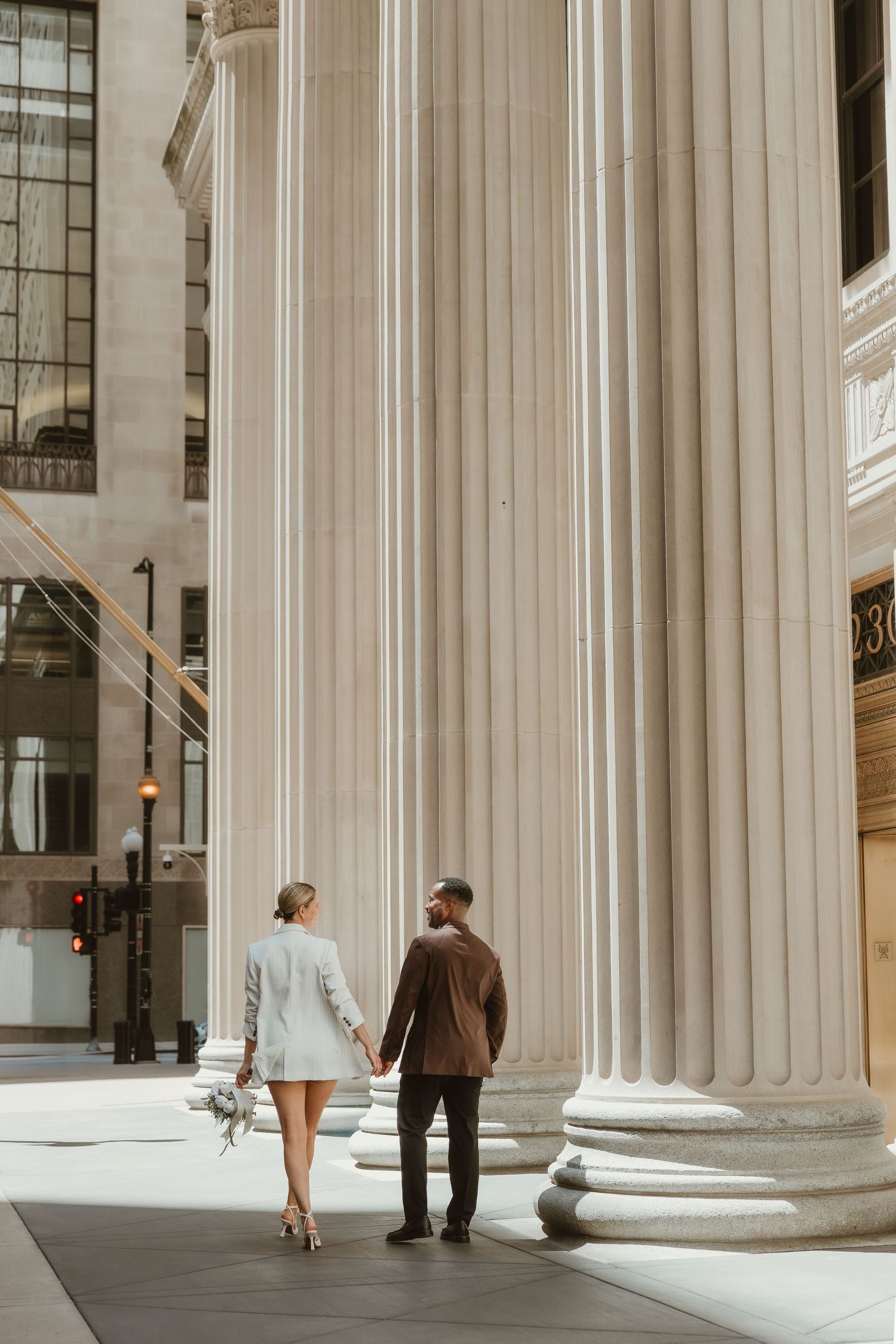 Modern wedding couple walking past classical columns in Chicago, IL, captured by local photographer specializing in editorial portraits