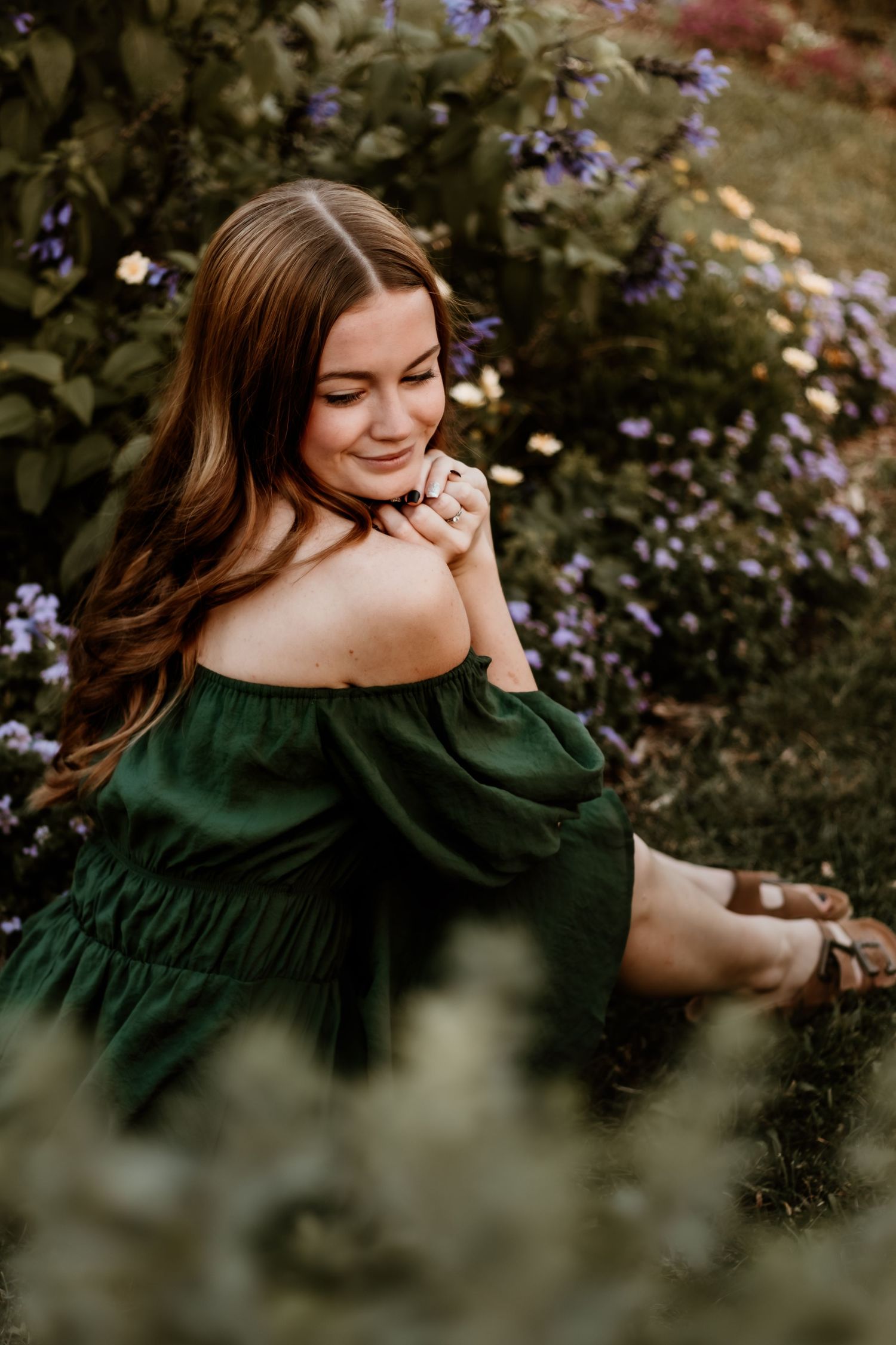 High school senior holds hands together and looks over shoulder to pose within the flowers