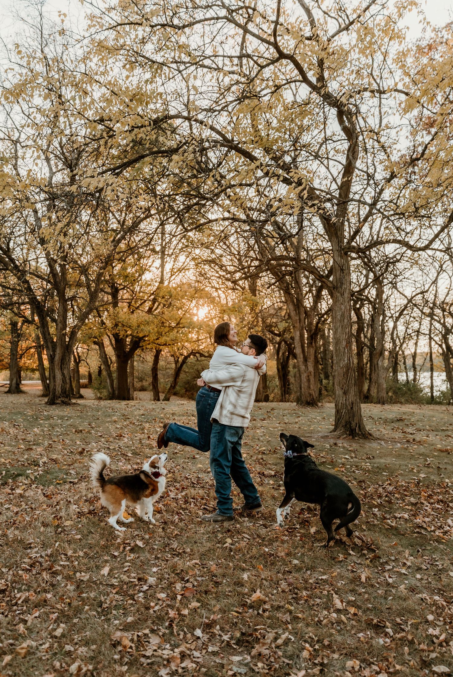 Boyfriend swinging girlfriend in the air while their dogs run around them in front of the sunset for a family photo session