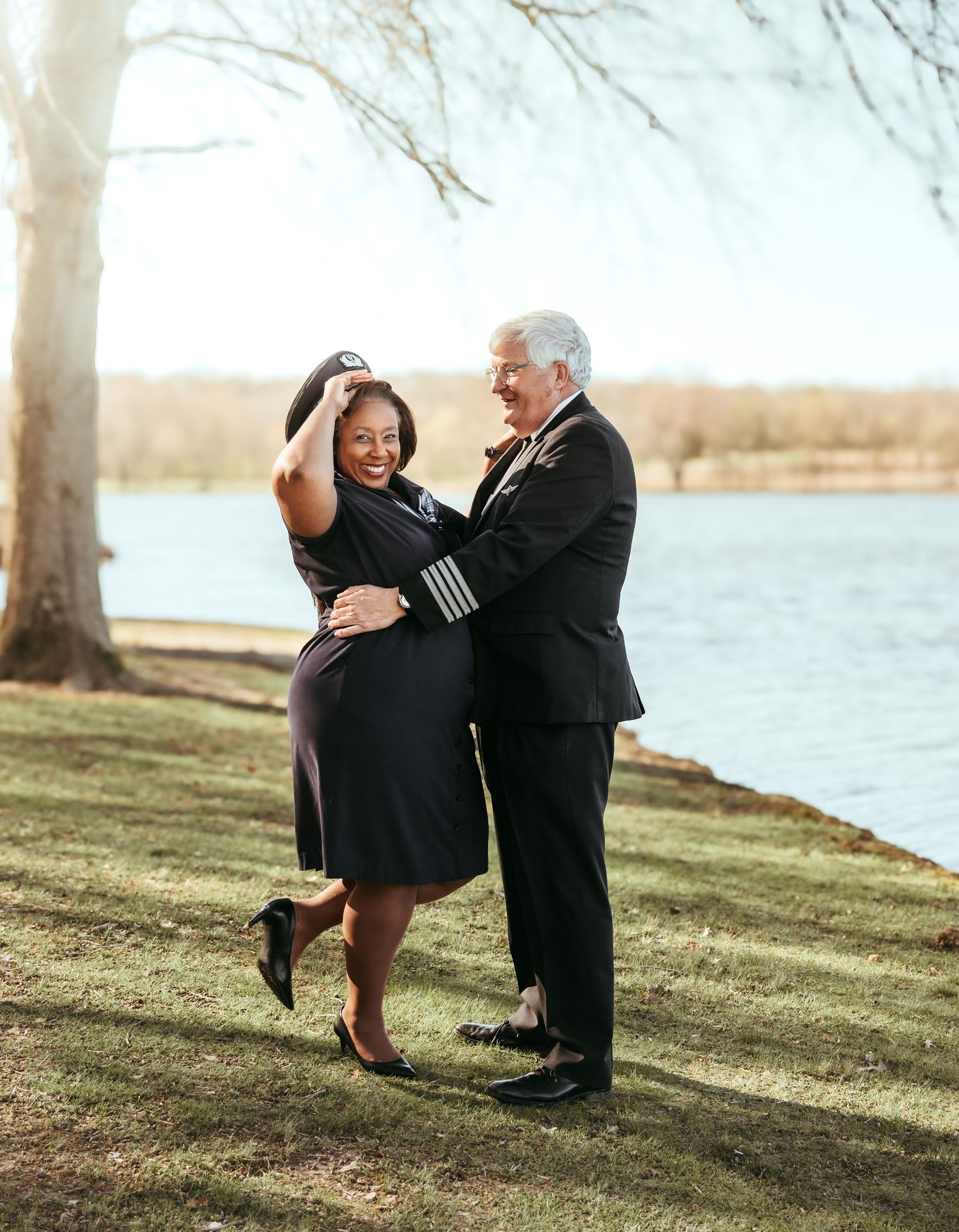 Couple posing in their pilot and flight attendant uniforms in front of the lake for their engagement session