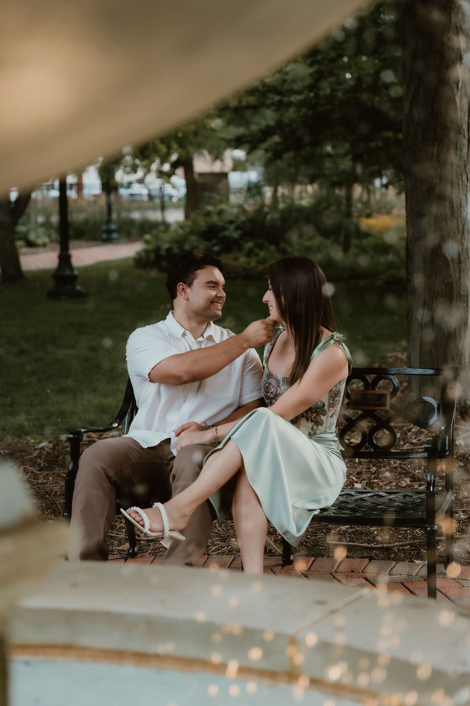 Groom lightly touches brides chin while having an intimate moment in a garden setting with a fountain during golden hour