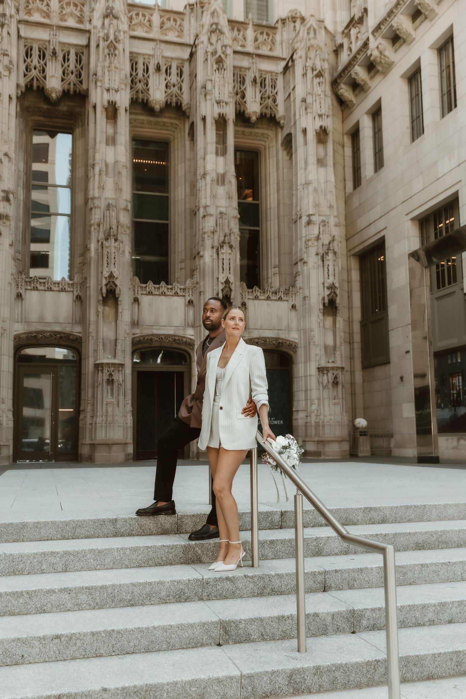 Chic wedding couple on stone steps in Chicago, IL,posing in front of Gothic-style architecture, captured by a local bloomington photographer
